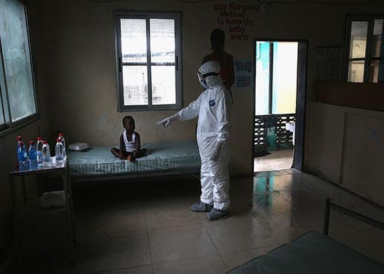 A Liberian Ministry of Health worker, dressed in an anti-contamination suit, speaks to Banu, 4, in a holding center for suspected Ebola patients.