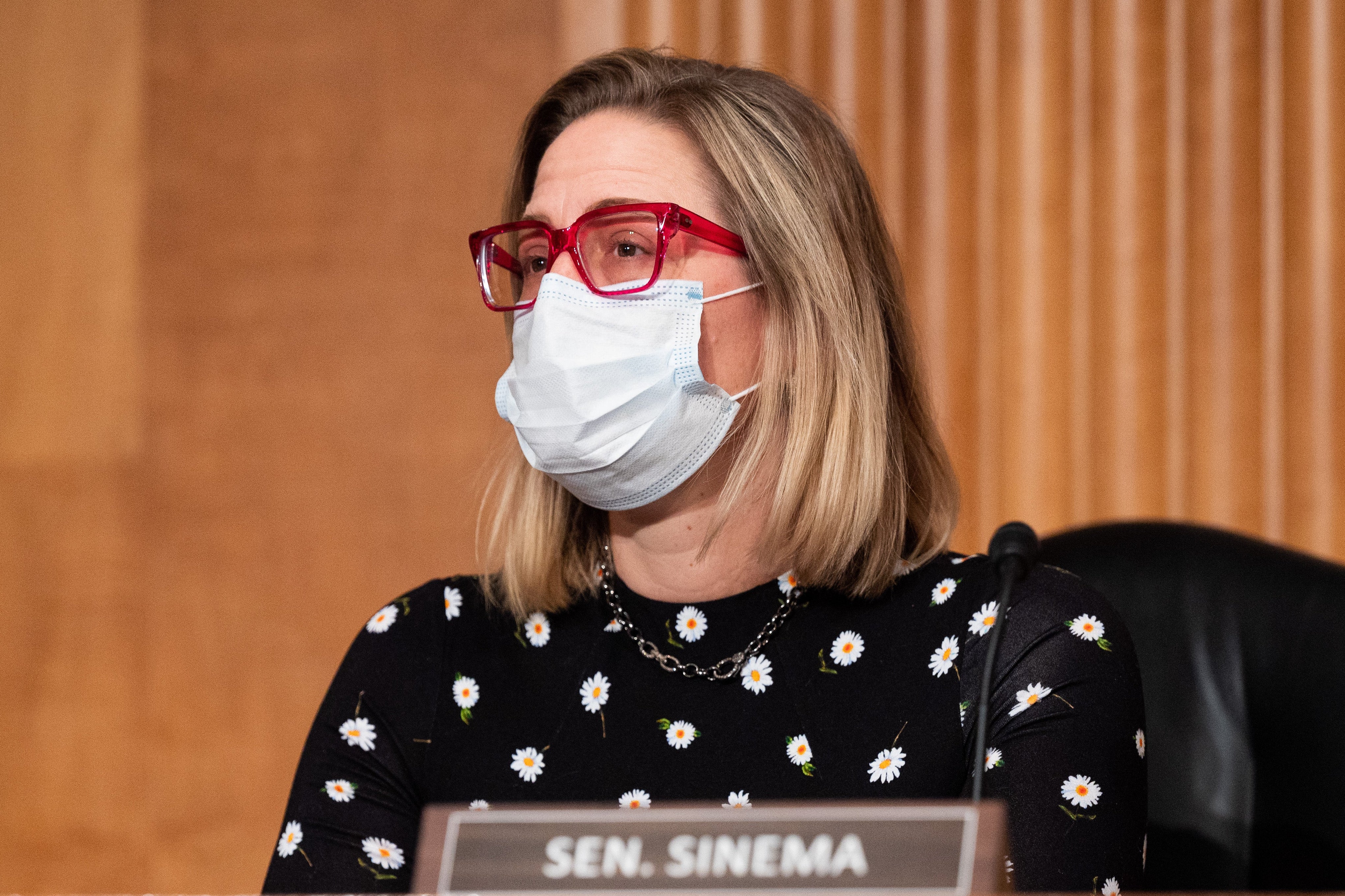Sen. Kyrsten Sinema in a mask at a dais with a name placard in front of her