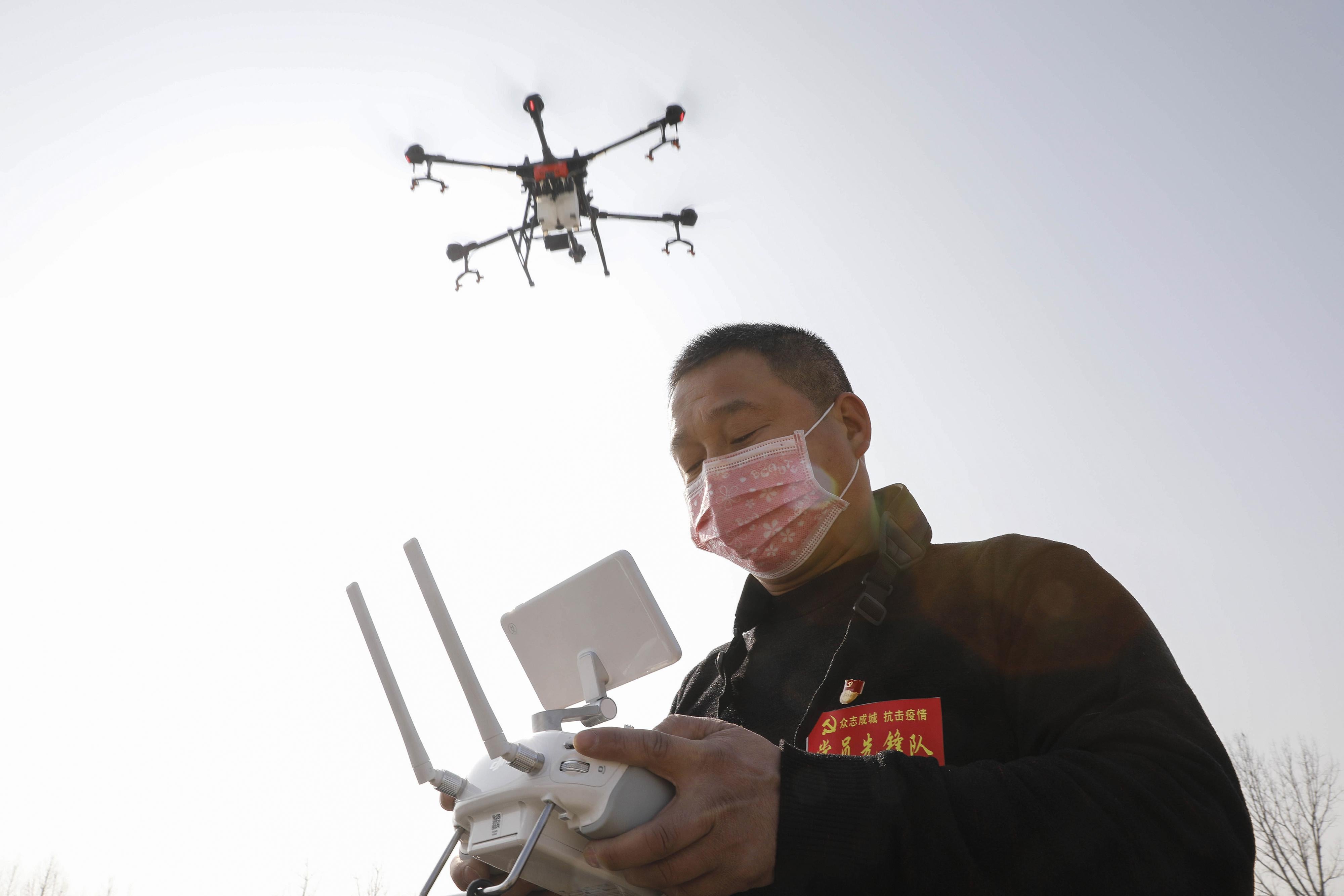 A man wearing a face mask operates a drone flying in the sky.