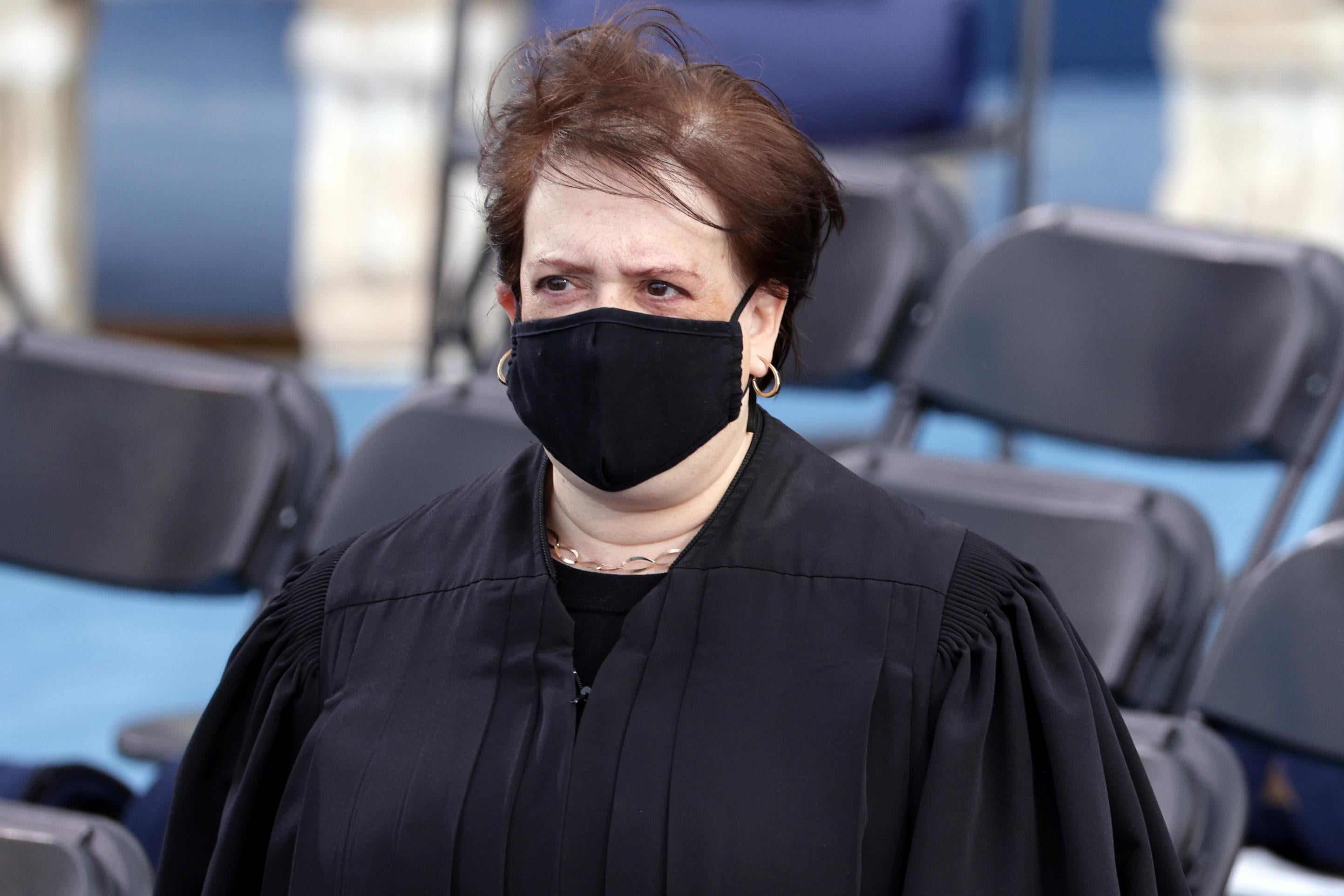 Elena Kagan stands outside wearing a robe and a mask.