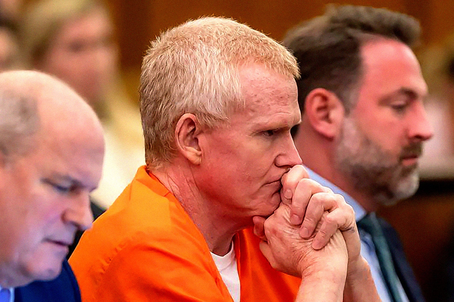 Alex Murdaugh in an orange prison jumpsuit at the trial with his chin on his clasped hands.