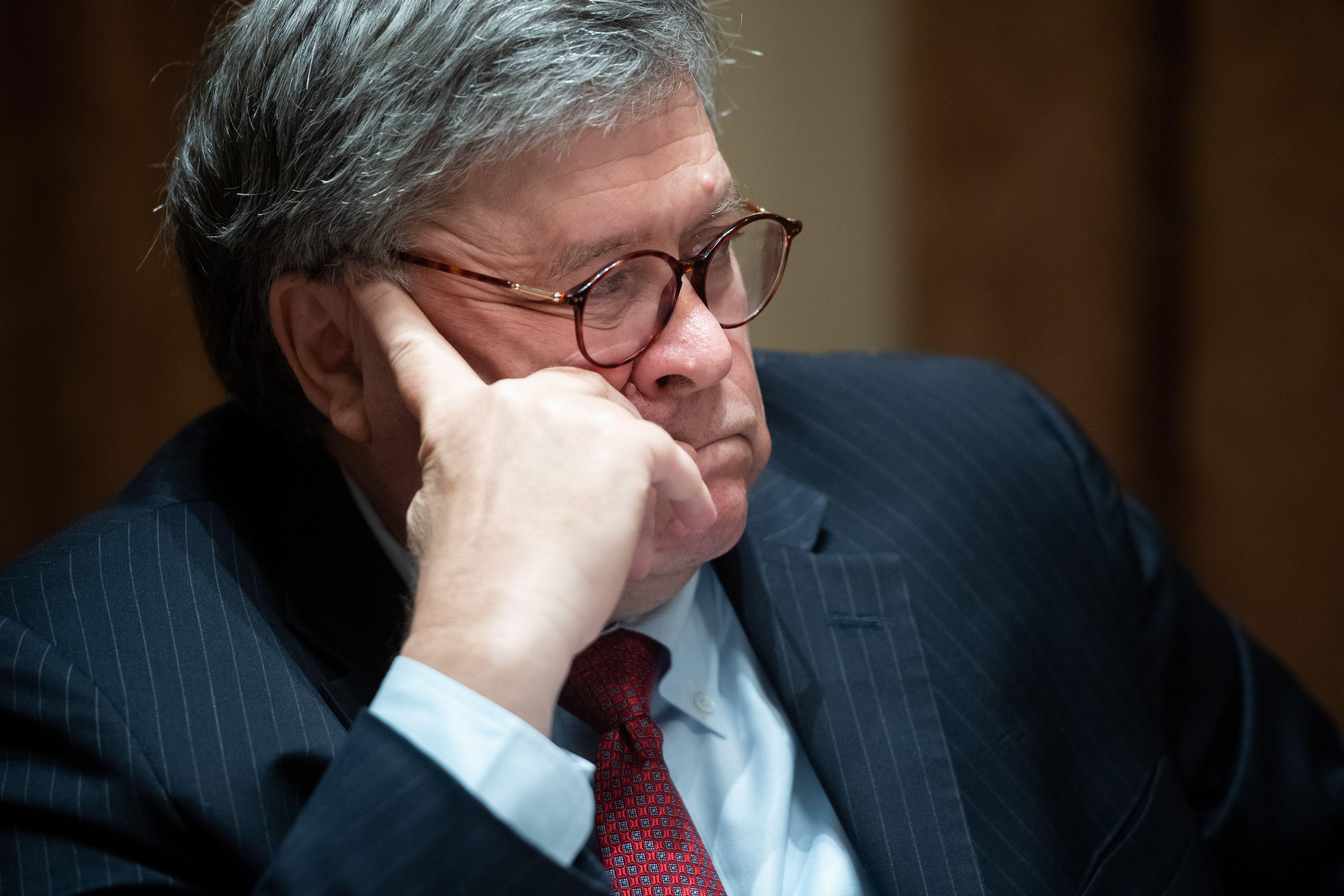 Bill Barr sits at a table, hand to his head.