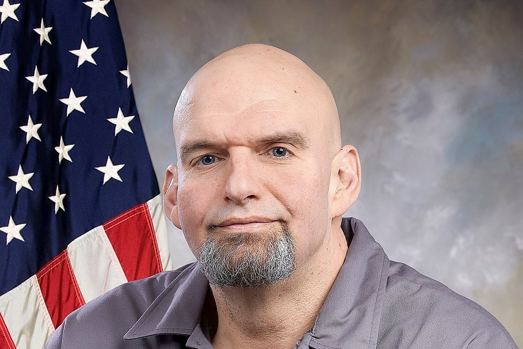 John Fetterman wearing a gray shirt, sitting in front of an American flag