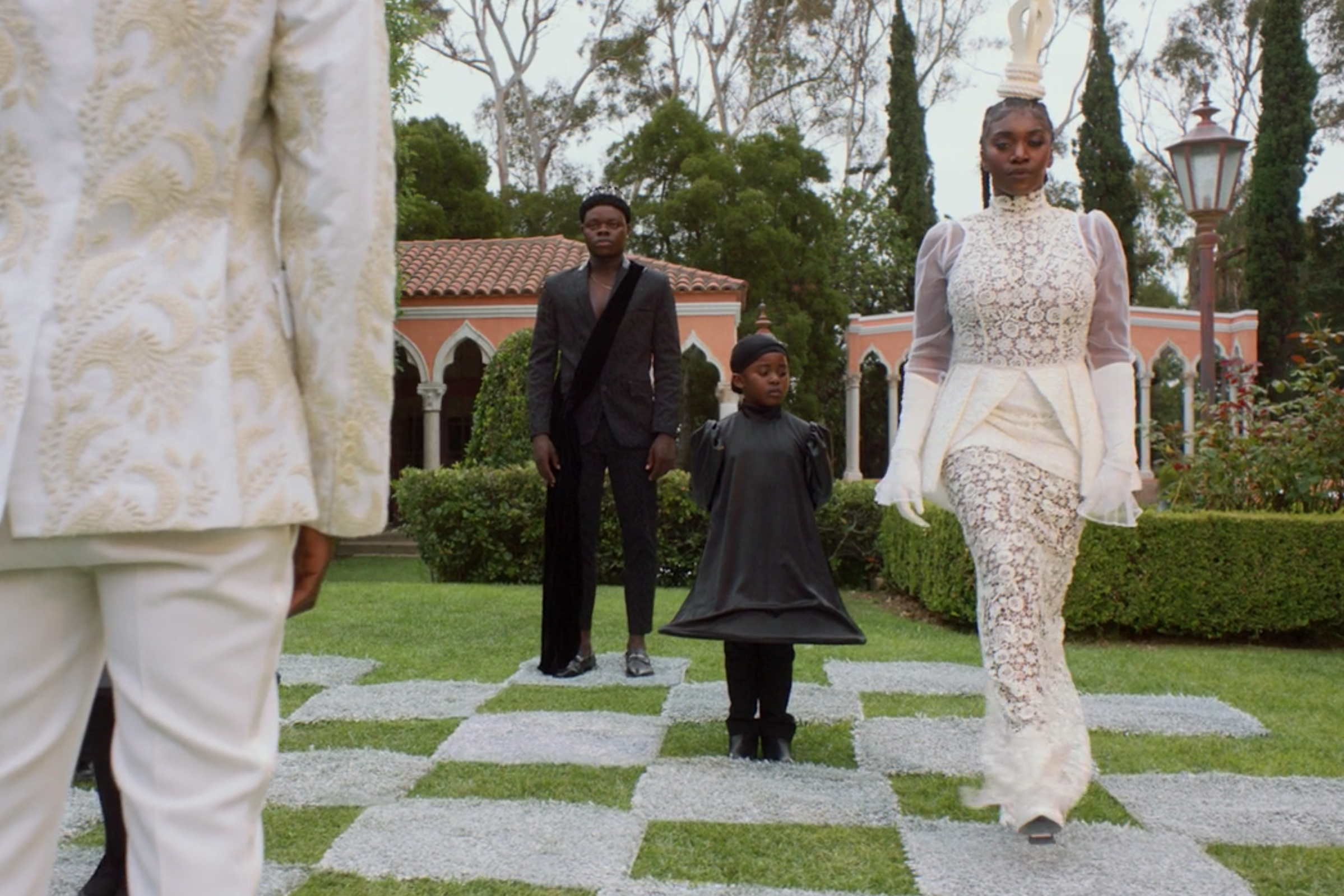 A woman dressed as a human chess piece walks away from two men dressed in black as chess pieces.