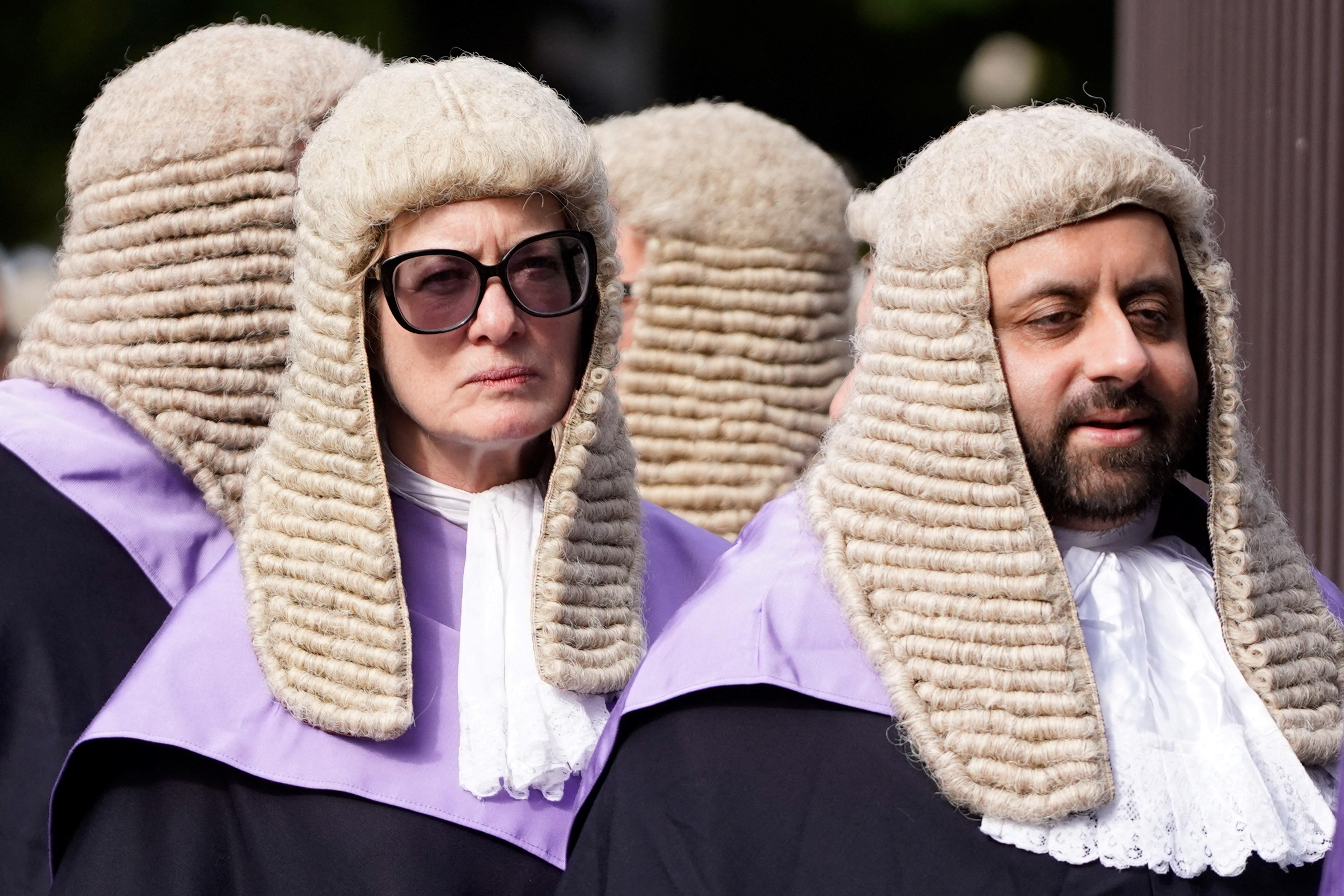 Judges process to the Palace of Westminster in central London, as part of a tradition to mark the start of the new legal year, on October 3, 2022. One lady in a barrister/English judge wig wearing sunglasses and scowling, next to bearded dude in the barrister/English judge wig grinning.