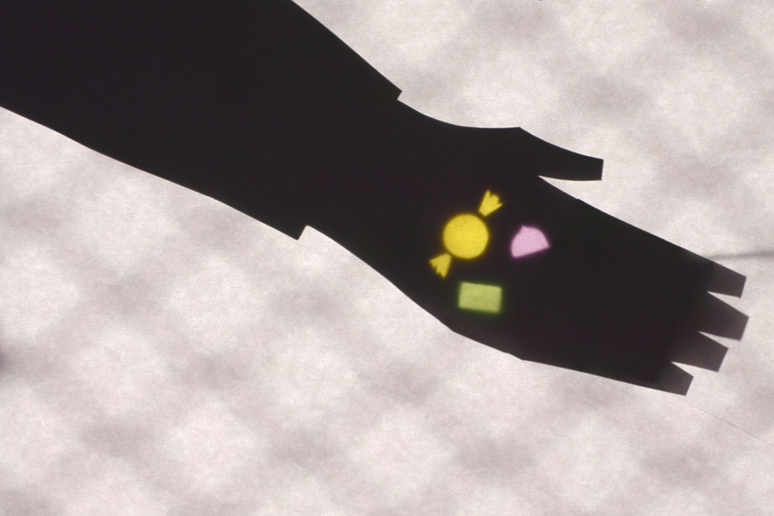 A shadow puppet hand holds out its palm with multicolored pieces of candy in it. 