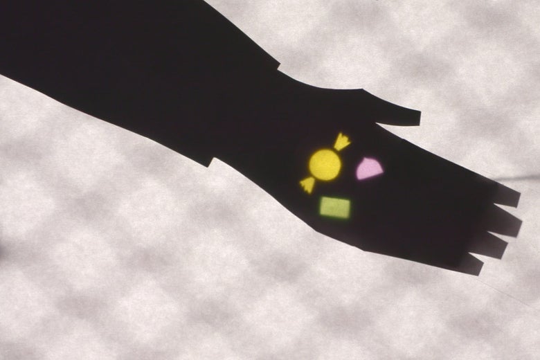 A shadow puppet hand holds out its palm with multicolored pieces of candy in it.
