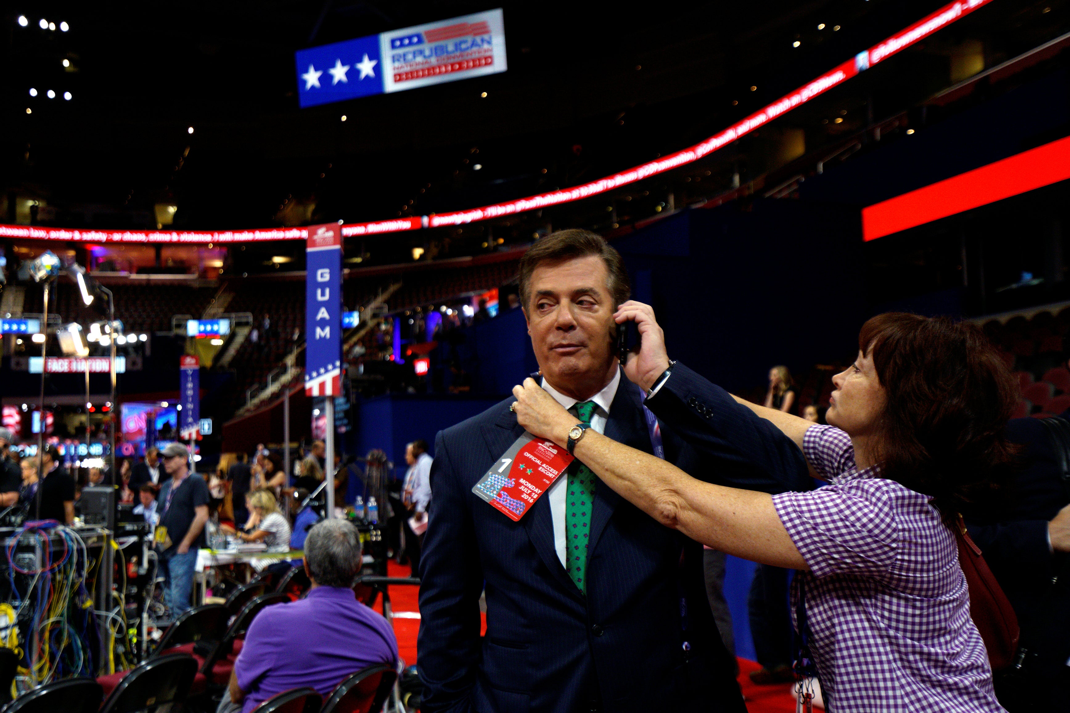 Manafort holds a cell phone to his ear as a credential is placed around his neck while he stands on the convention floor.