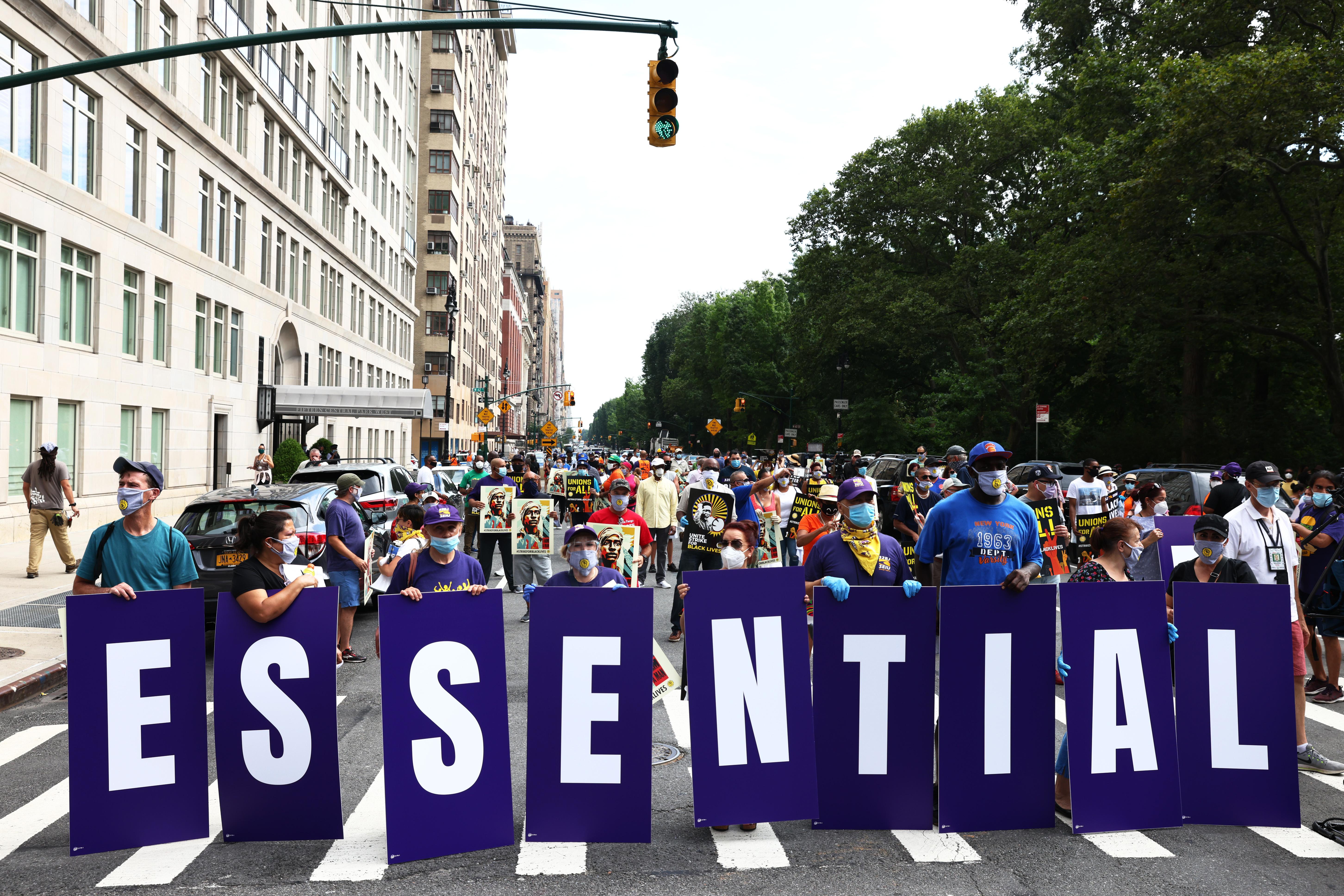Members of the 32BJ union hold up signs spelling out "Essential Workers" during a "Strike for Black Lives" rally.