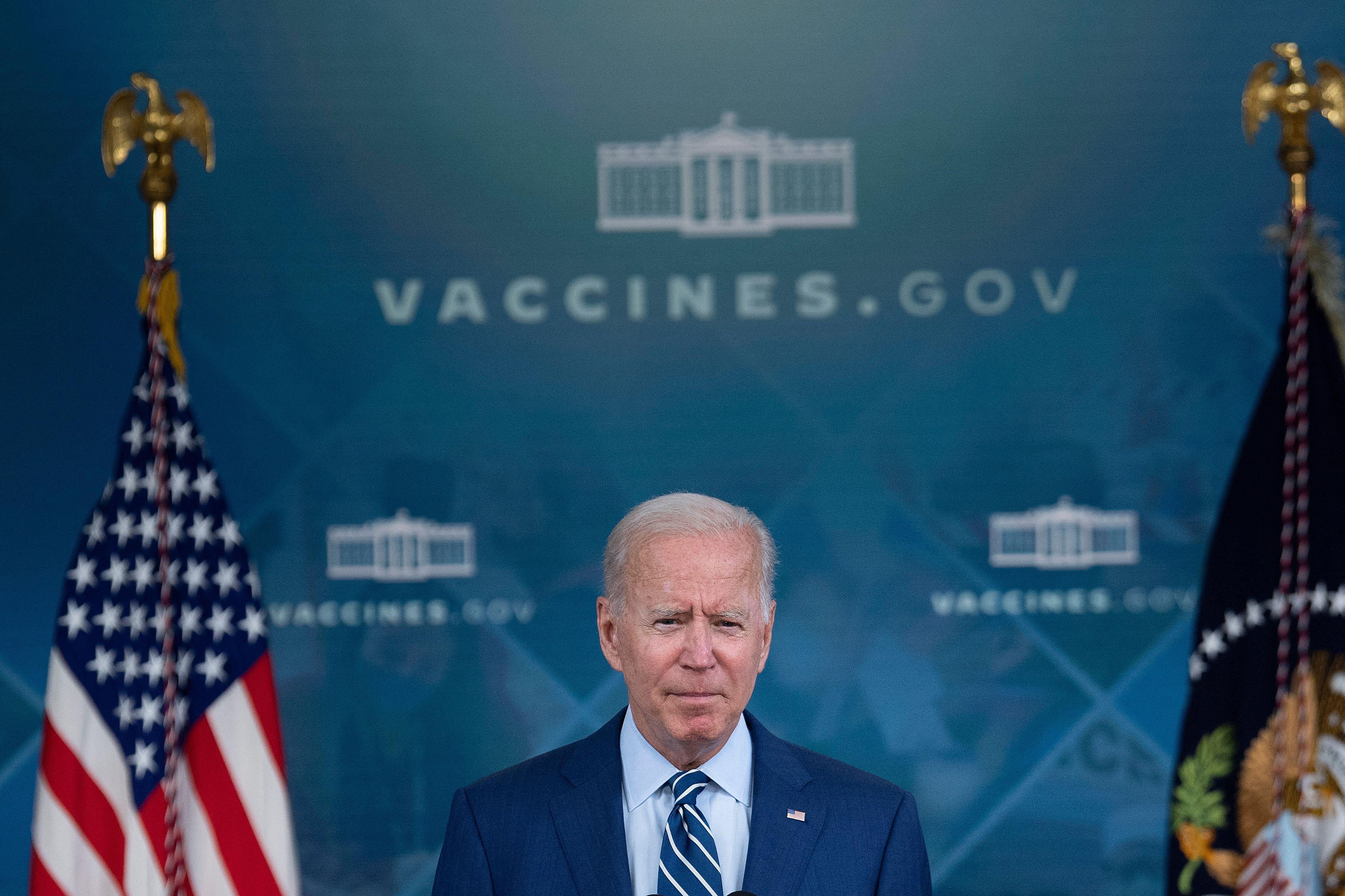 Biden stands in front of an American flag, a presidential flag, and a backdrop that says vaccines.gov