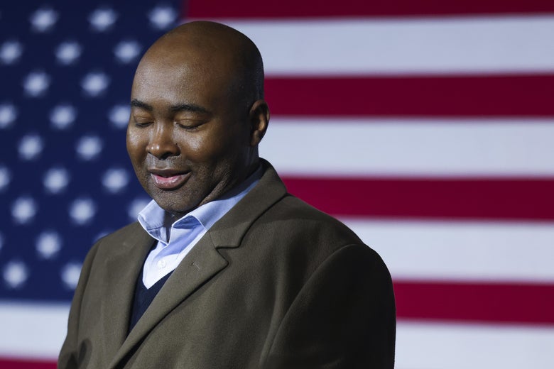 Jaime Harrison looks down as he stands in front of a U.S. flag.