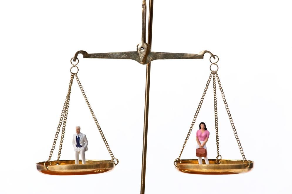 Image of a scale with a man on a slightly more weighted scale than the other scale holding a woman