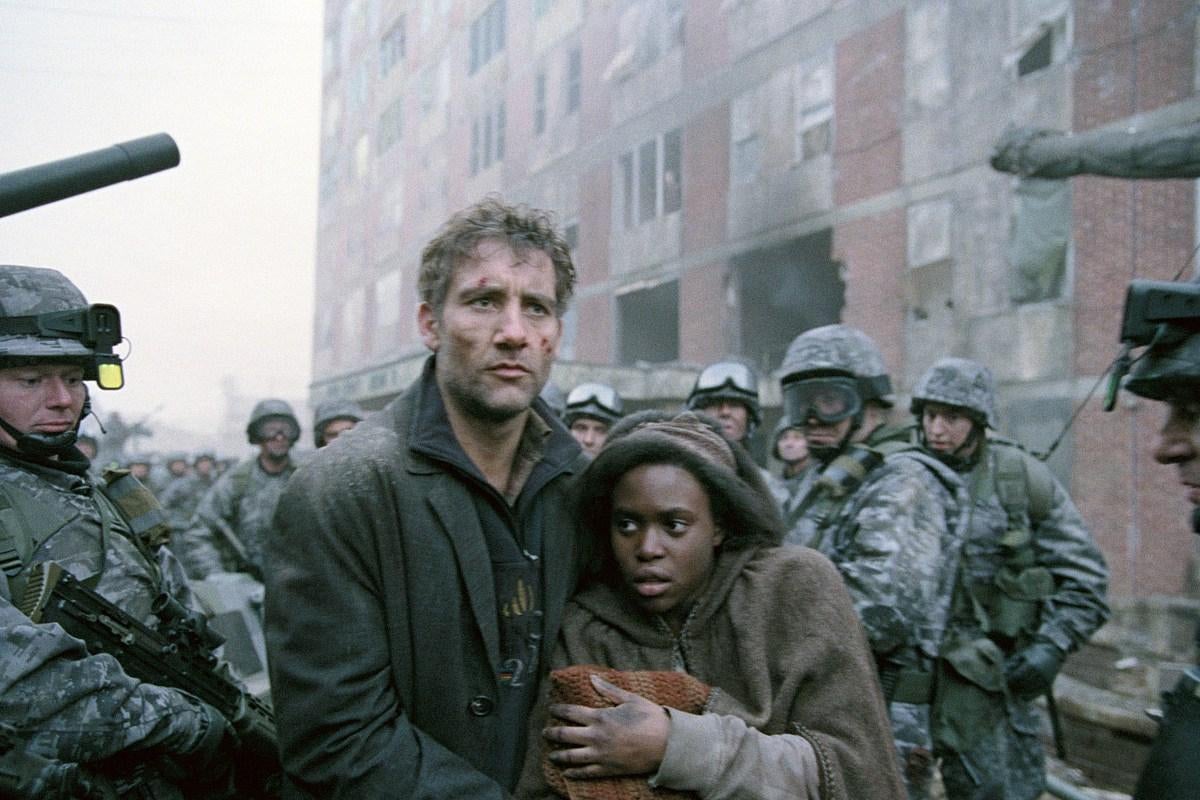 A battered Clive Owen ushers a hooded Black woman carrying a baby through a crowd of militia. 