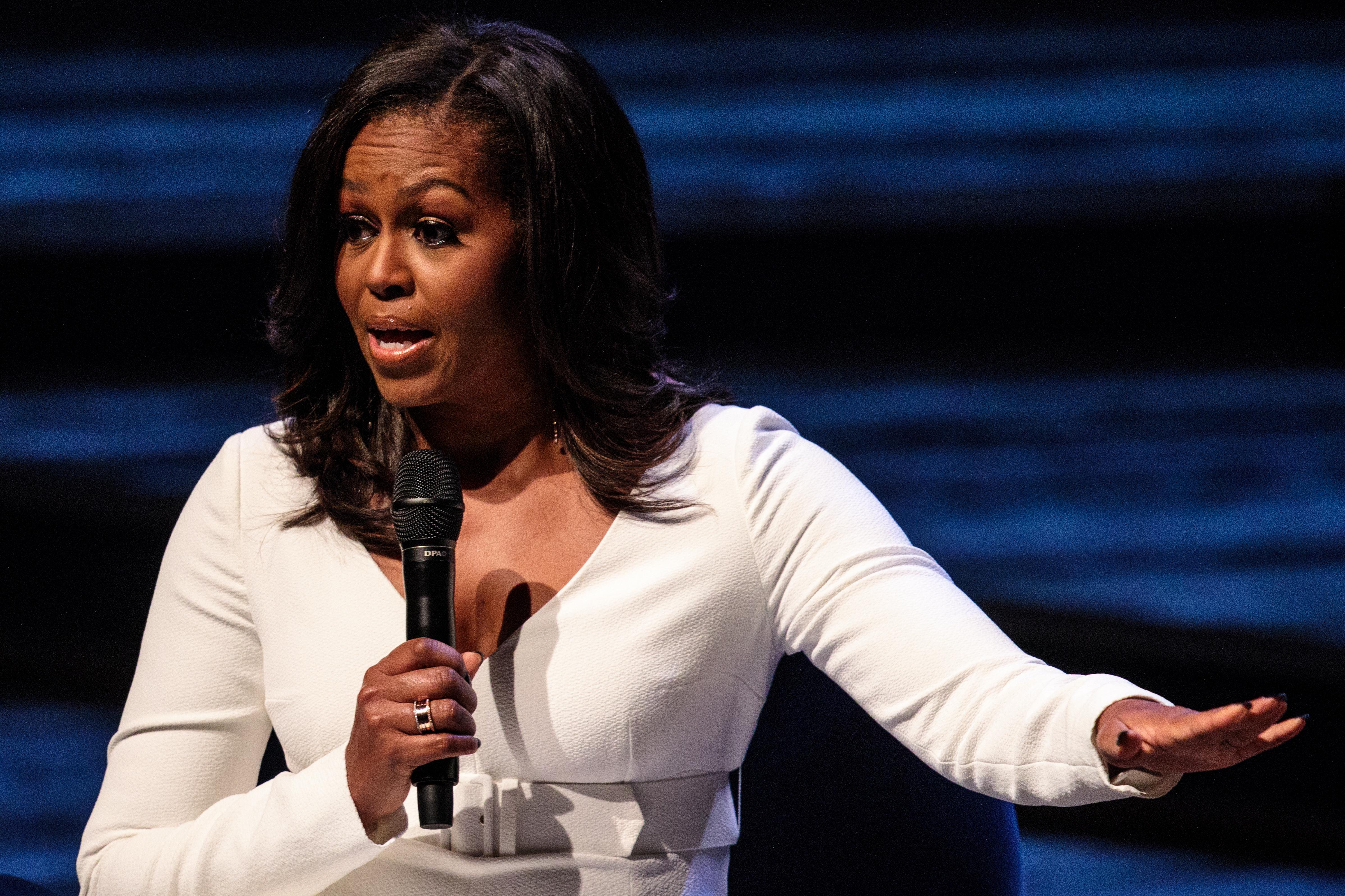 Former U.S. First Lady Michelle Obama speaks onstage, wearing a white pantsuit