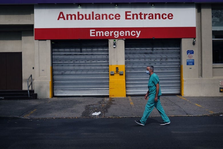 A man with short graying hair walks past a pair of garage doors below a sign that reads "Ambulance Entrance, Emergency."