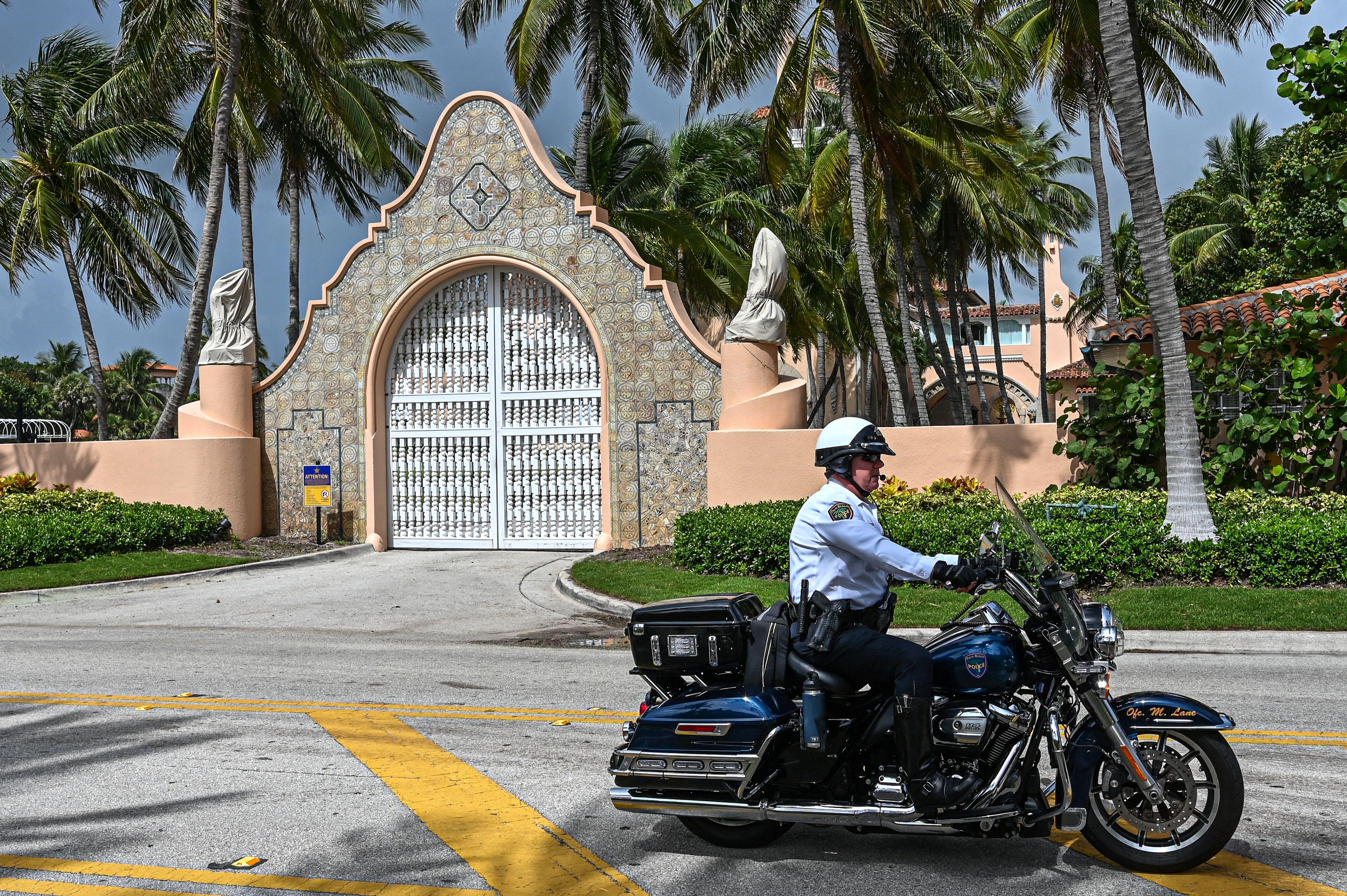 An officer on a motorcycle sits in front of the gated entrance to Mar-a-Lago.