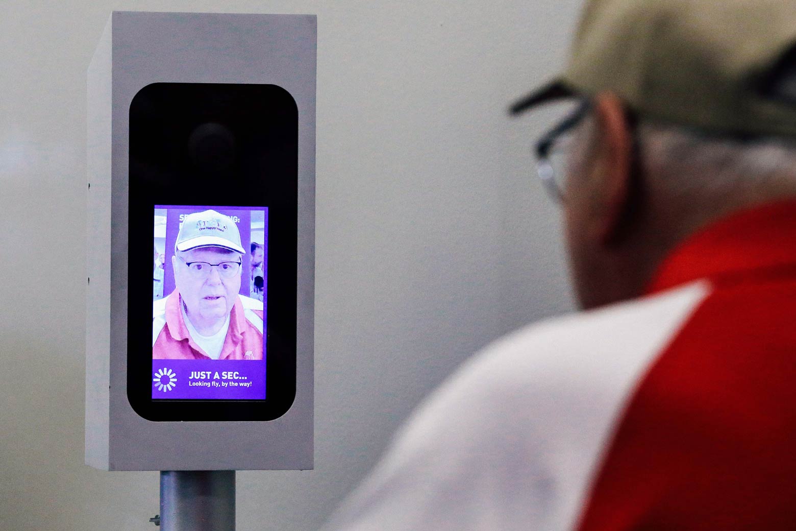 A man in a baseball cap and glasses looks into a screen on which an image of his face has been captured.
