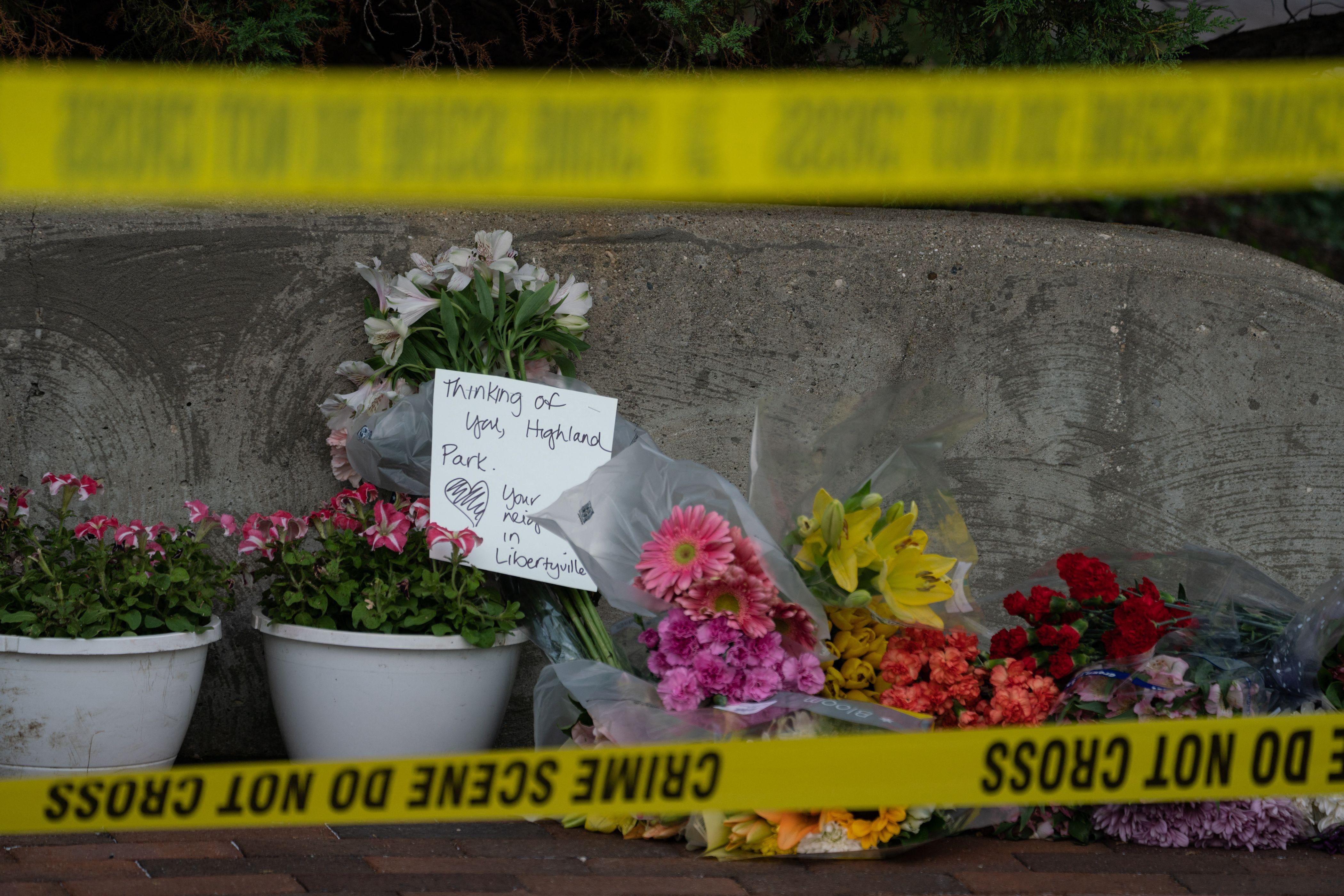 Bouquets of flowers laid on the grown, seen behind yellow police tape.