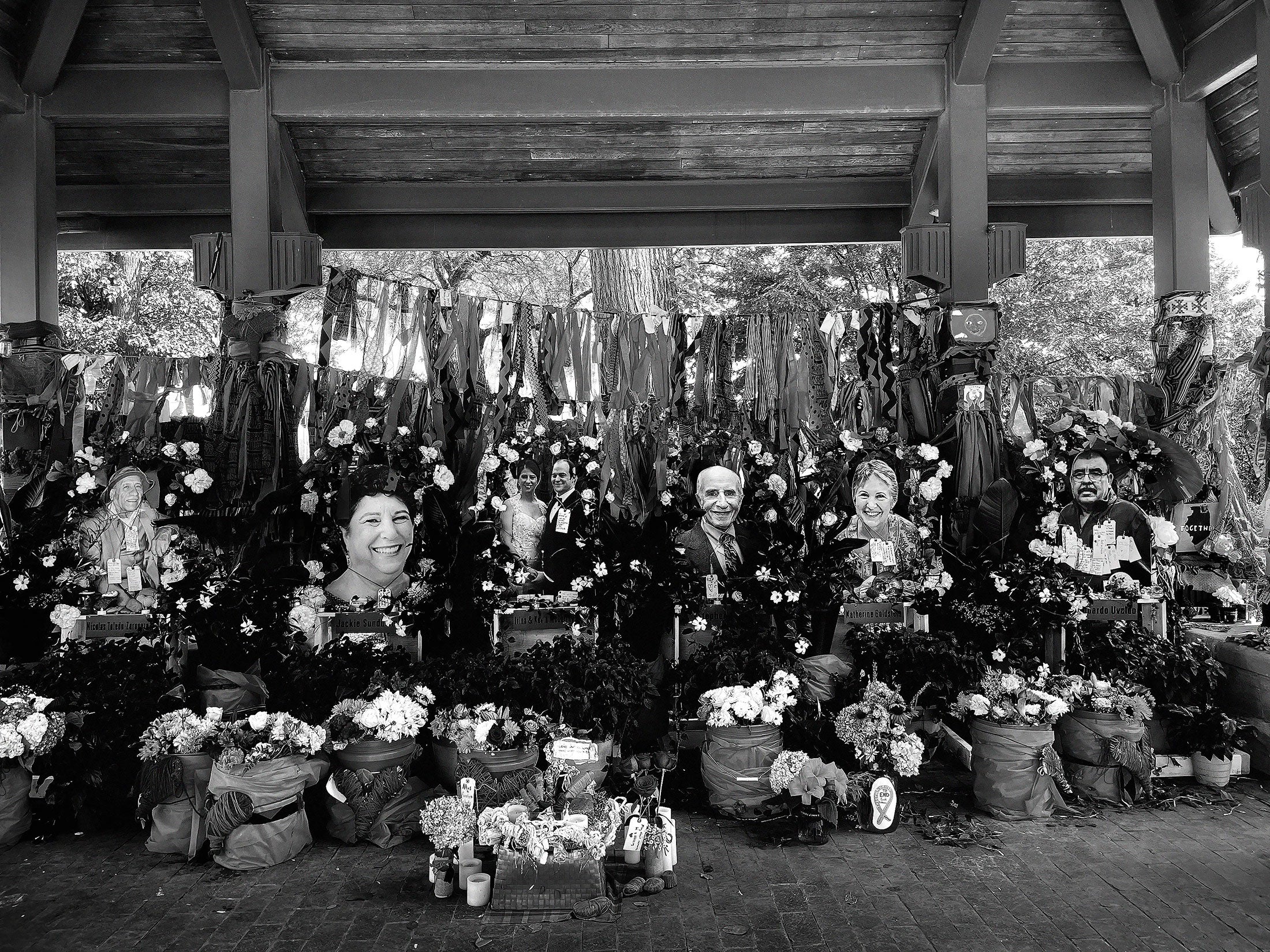 A black and white image of the memorial in Highland Park, where cardboard cutouts of the victims are covered in flowers.