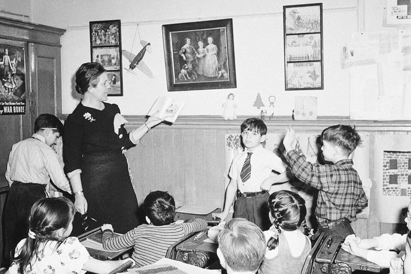 A black-and-white photo of a teacher holding a book in a class of young students.