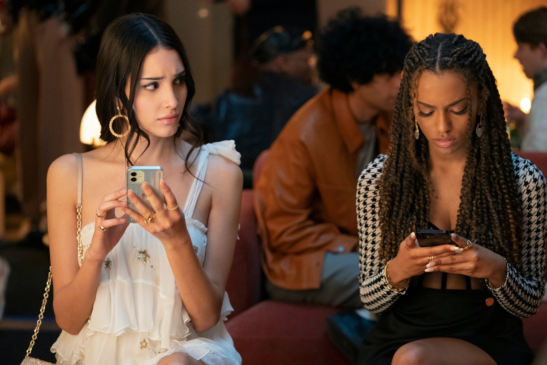 Two stylish young women on their phones at what appears to be a party