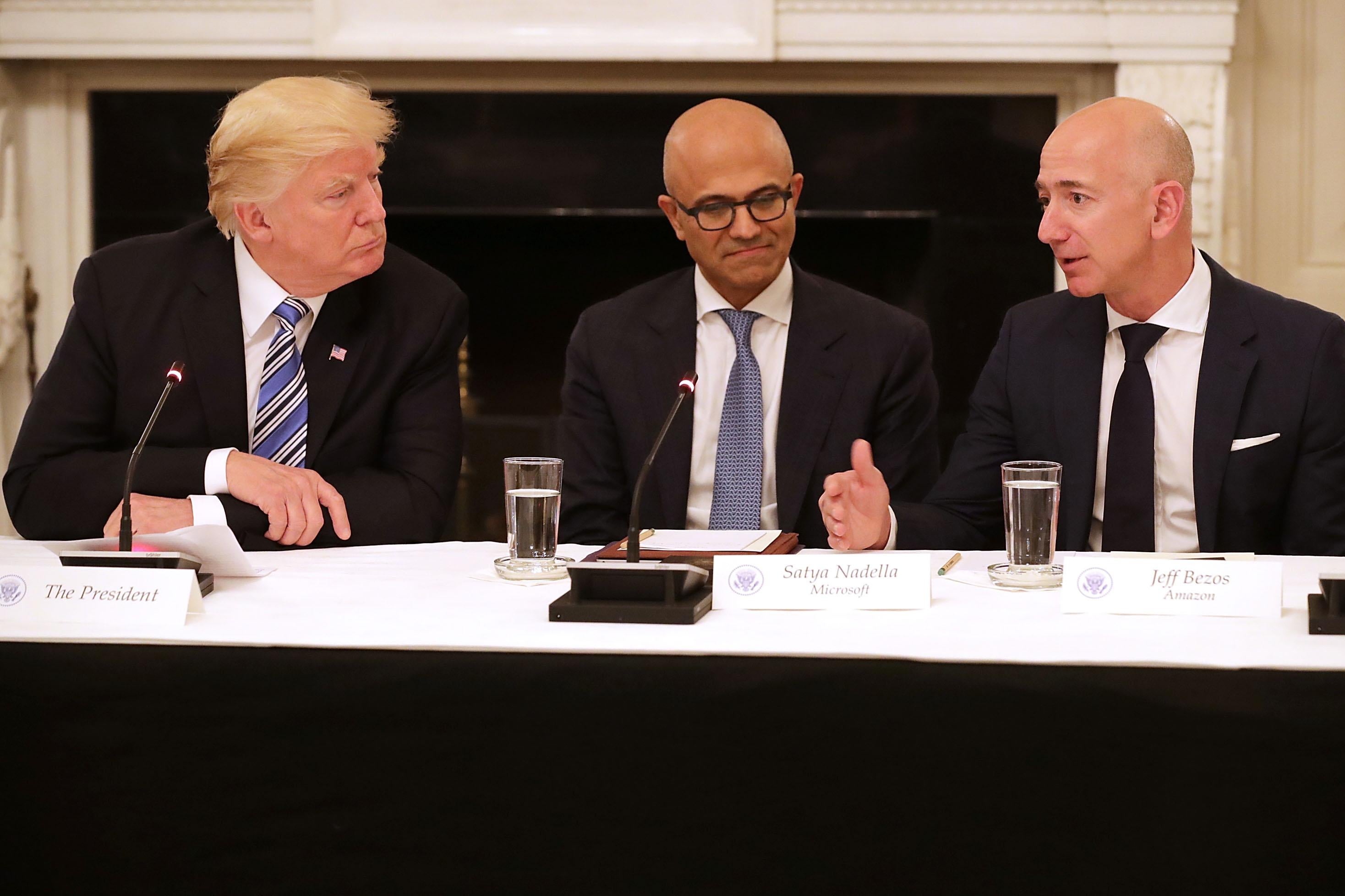 U.S. President Donald Trump, Microsoft CEO Satya Nadella, and Amazon CEO Jeff Bezos sit at a table.