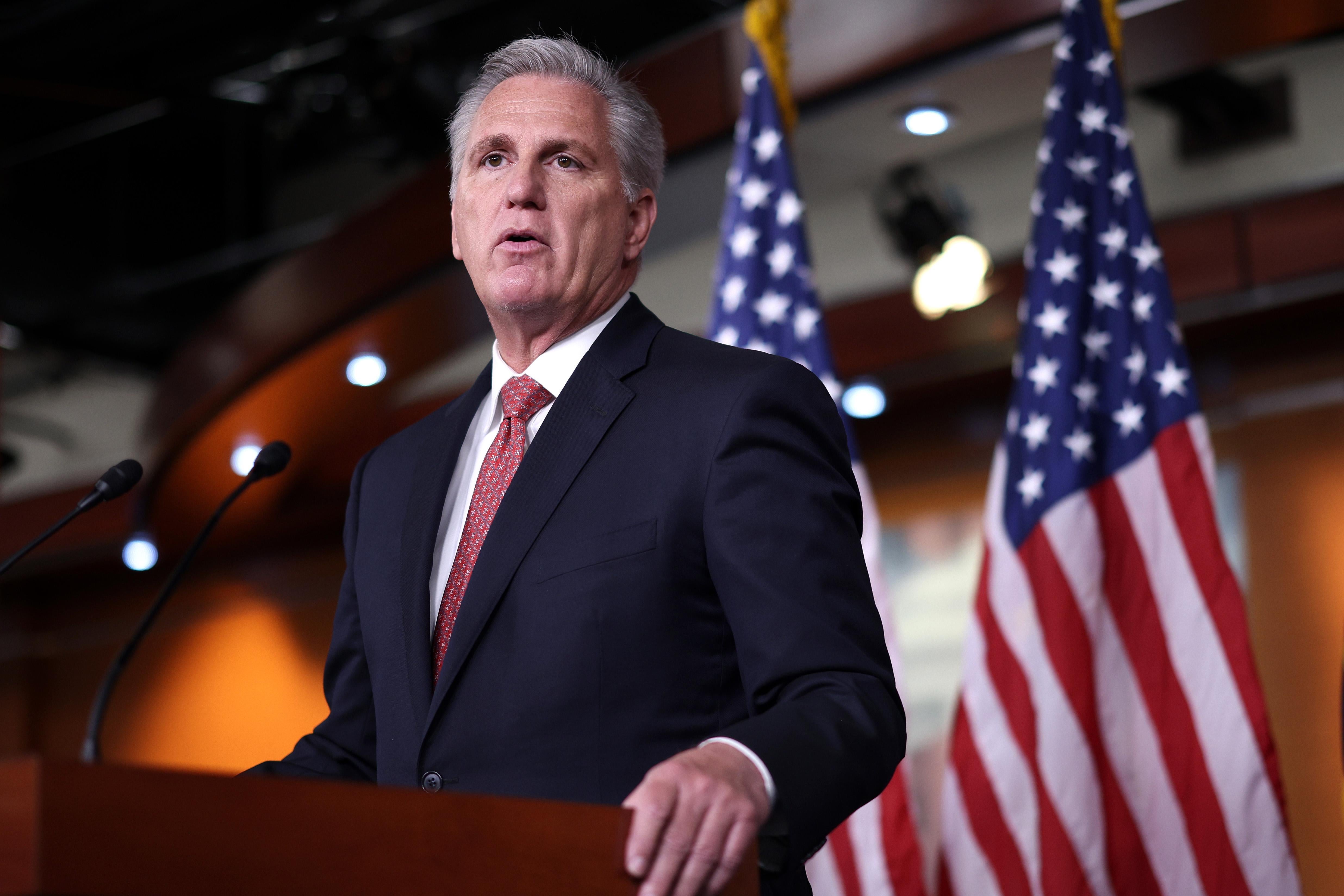 Kevin McCarthy behind a microphone, with some American flags in the background