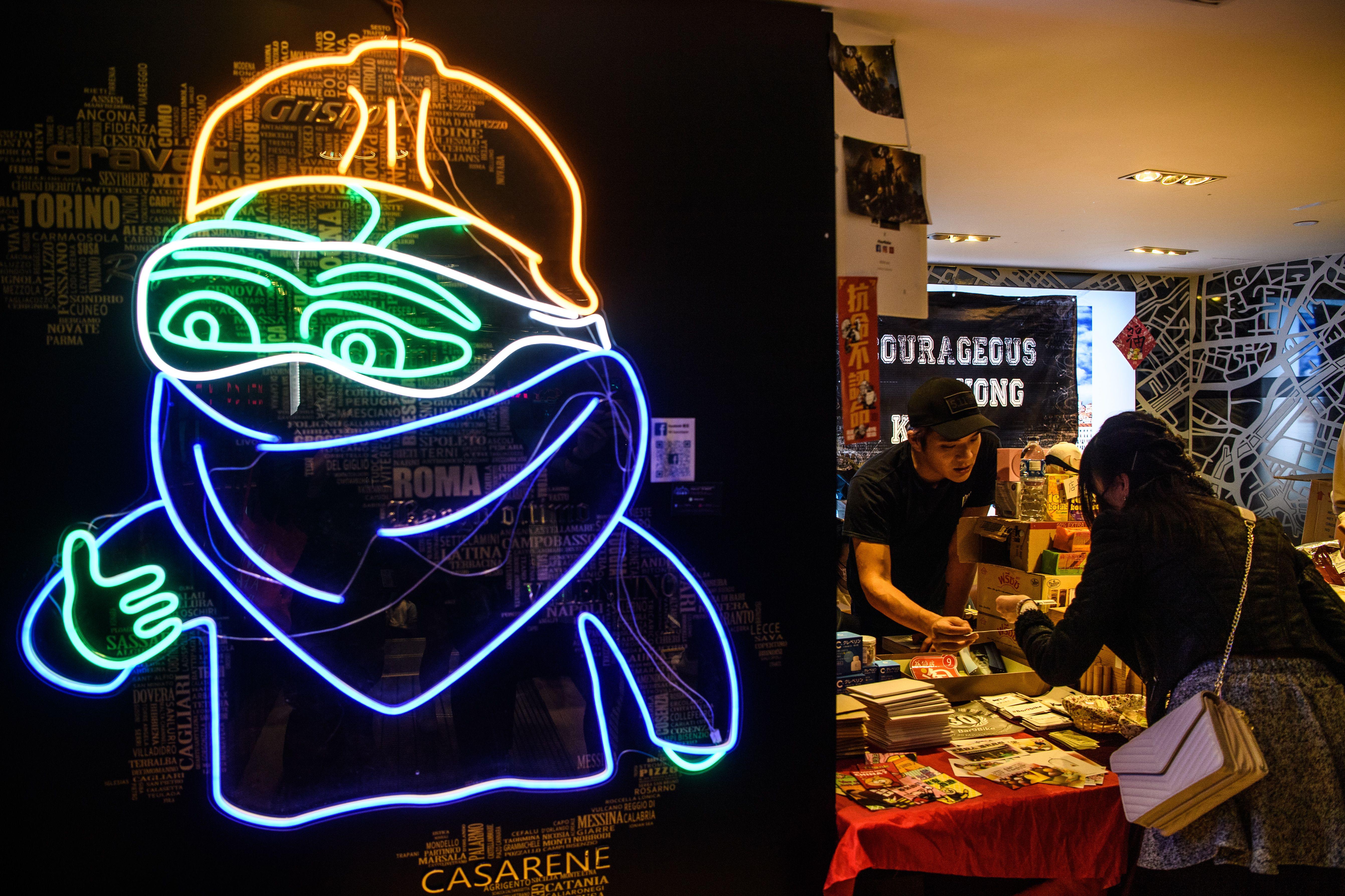In this picture taken on January 23, 2020, a neon sign depicting Pepe the Frog, a character used by pro-democracy activists as a symbol of their struggle in the Hong Kong protests, is displayed next to a stall set up as part of a pro-democracy themed Lunar New year market in a shopping mall in Hong Kong. (Photo by Anthony WALLACE / AFP) (Photo by ANTHONY WALLACE/AFP via Getty Images)