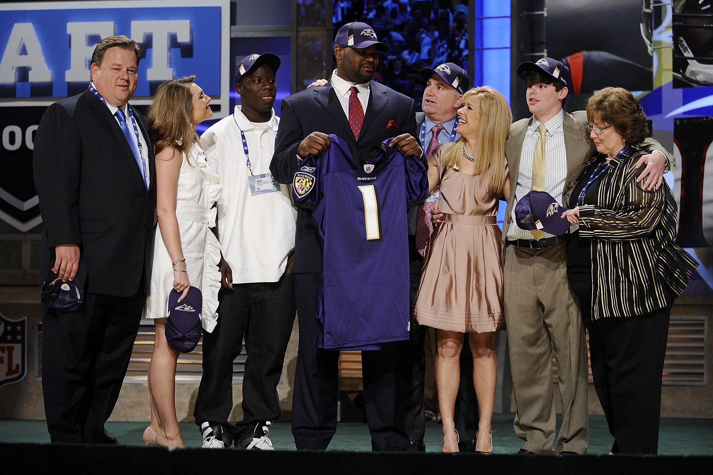 Michael Oher, at center, holds up a Baltimore Ravens jersey while surrounded by the Tuohys and others.