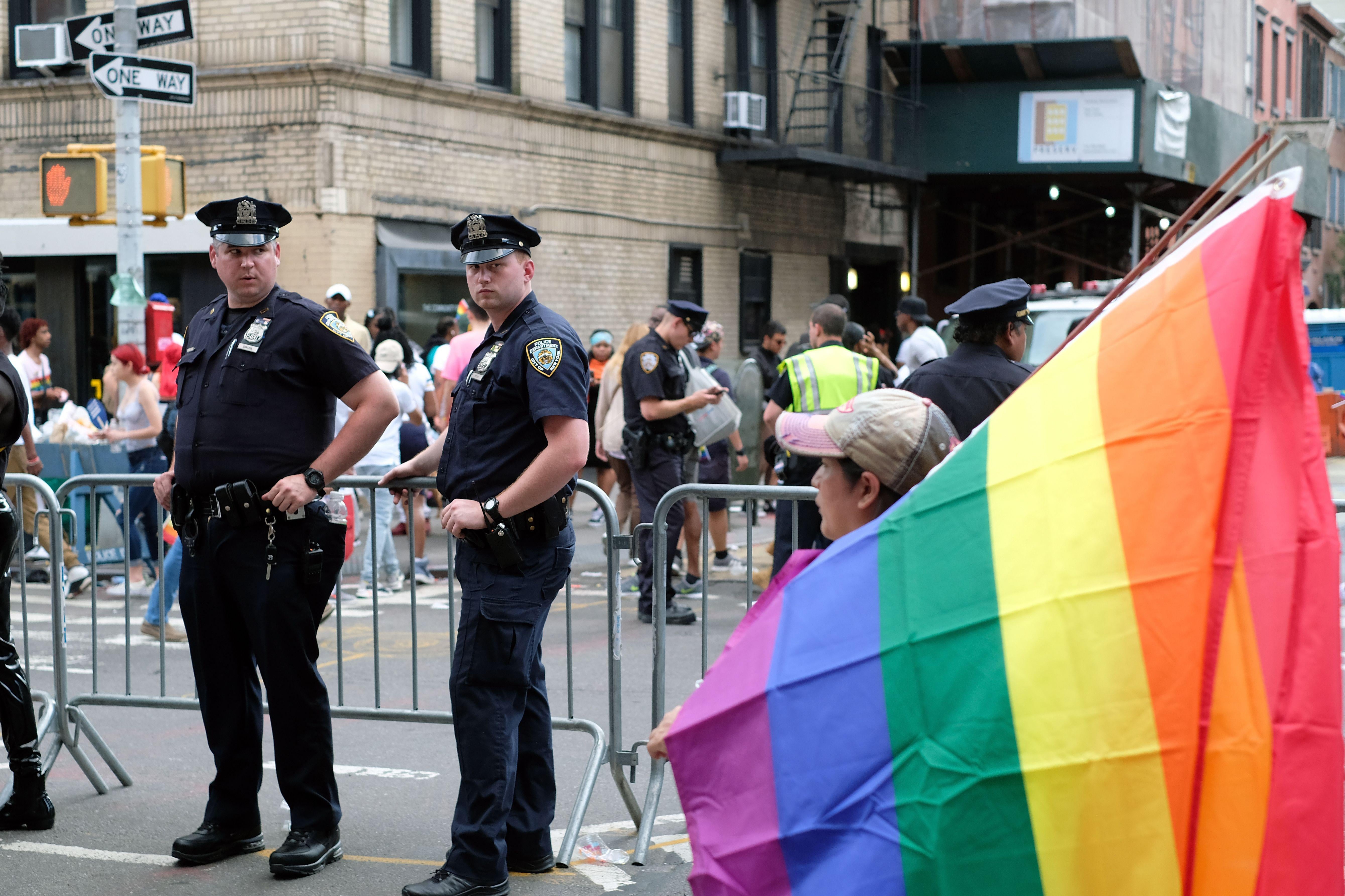 NYPD officers stand near pride flag in streets of New York.
