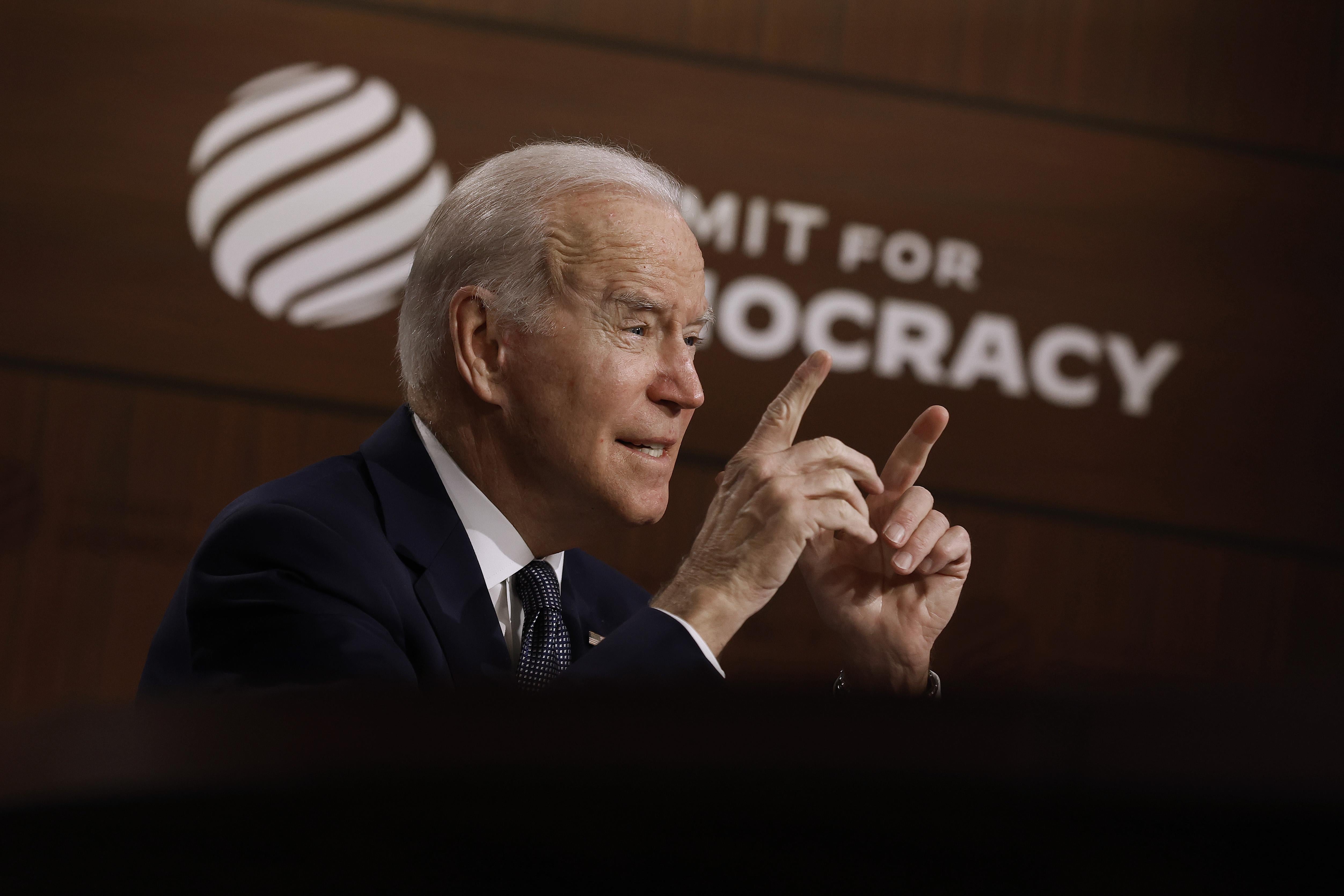 Biden gestures with both hands as he speaks in front of a backdrop that says "Summit for Democracy"
