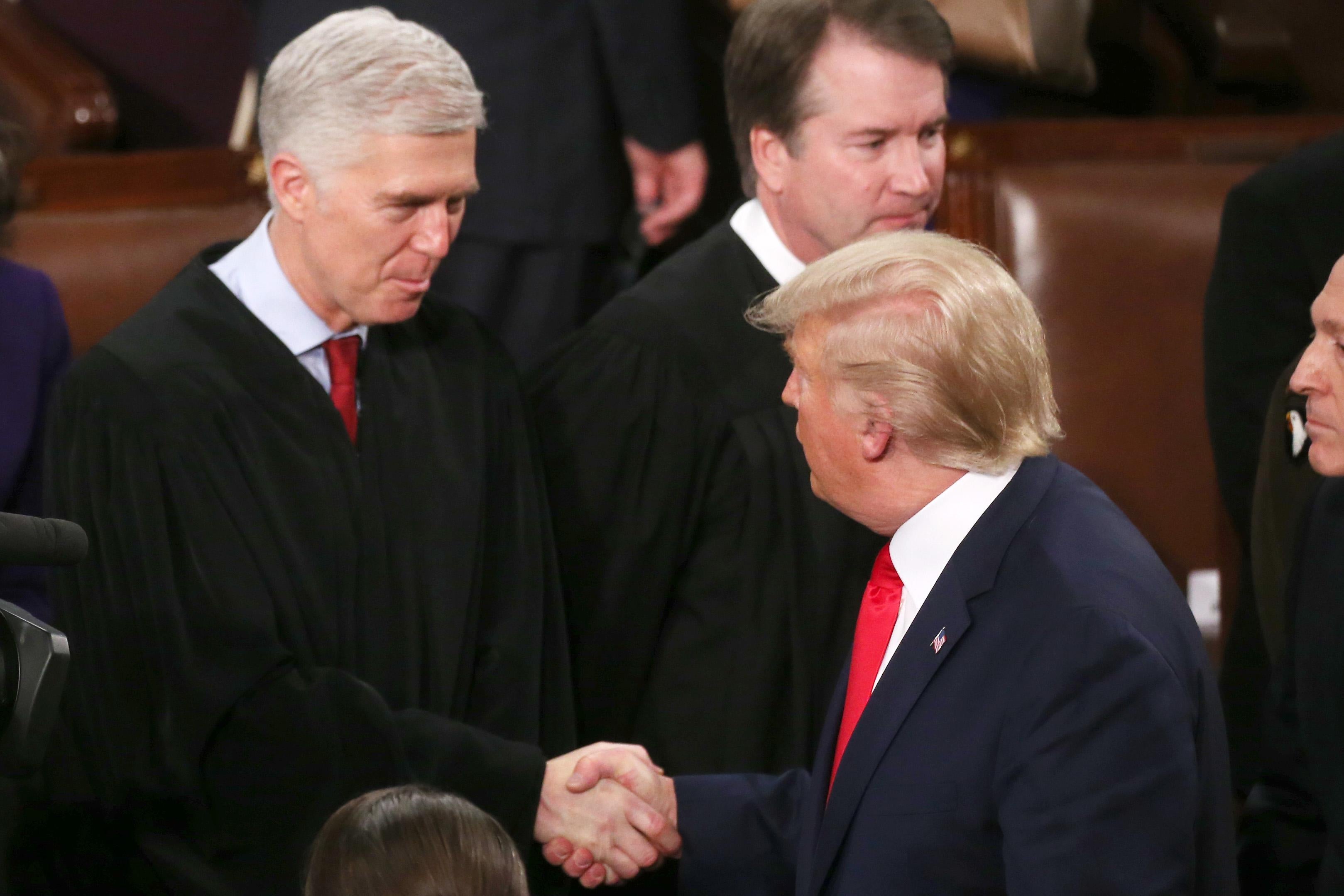 Trump shakes Gorsuch's hand while Brett Kavanaugh stands by.