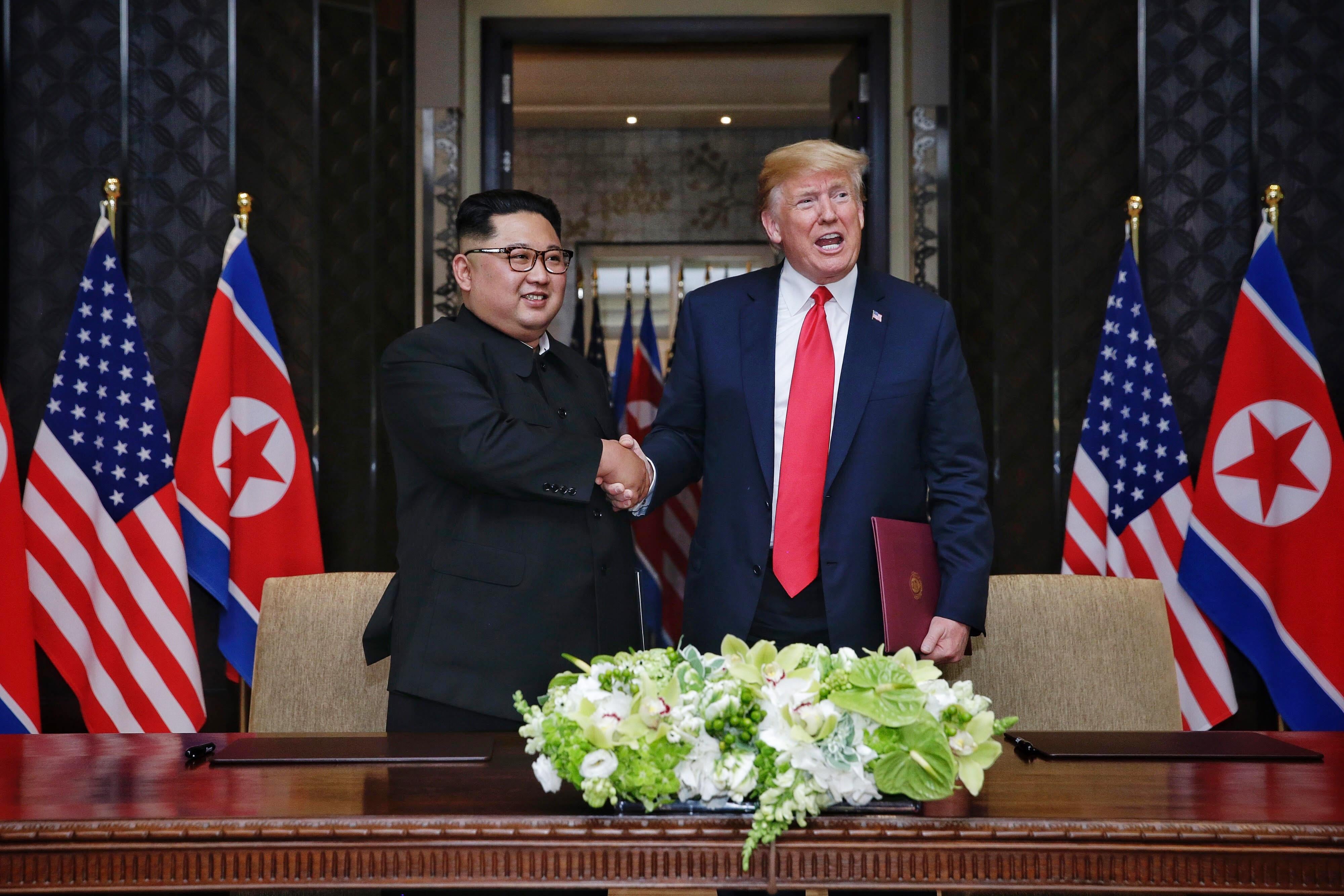 Kim Jong-un and President Trump shaking hands amid North Korean and American flags