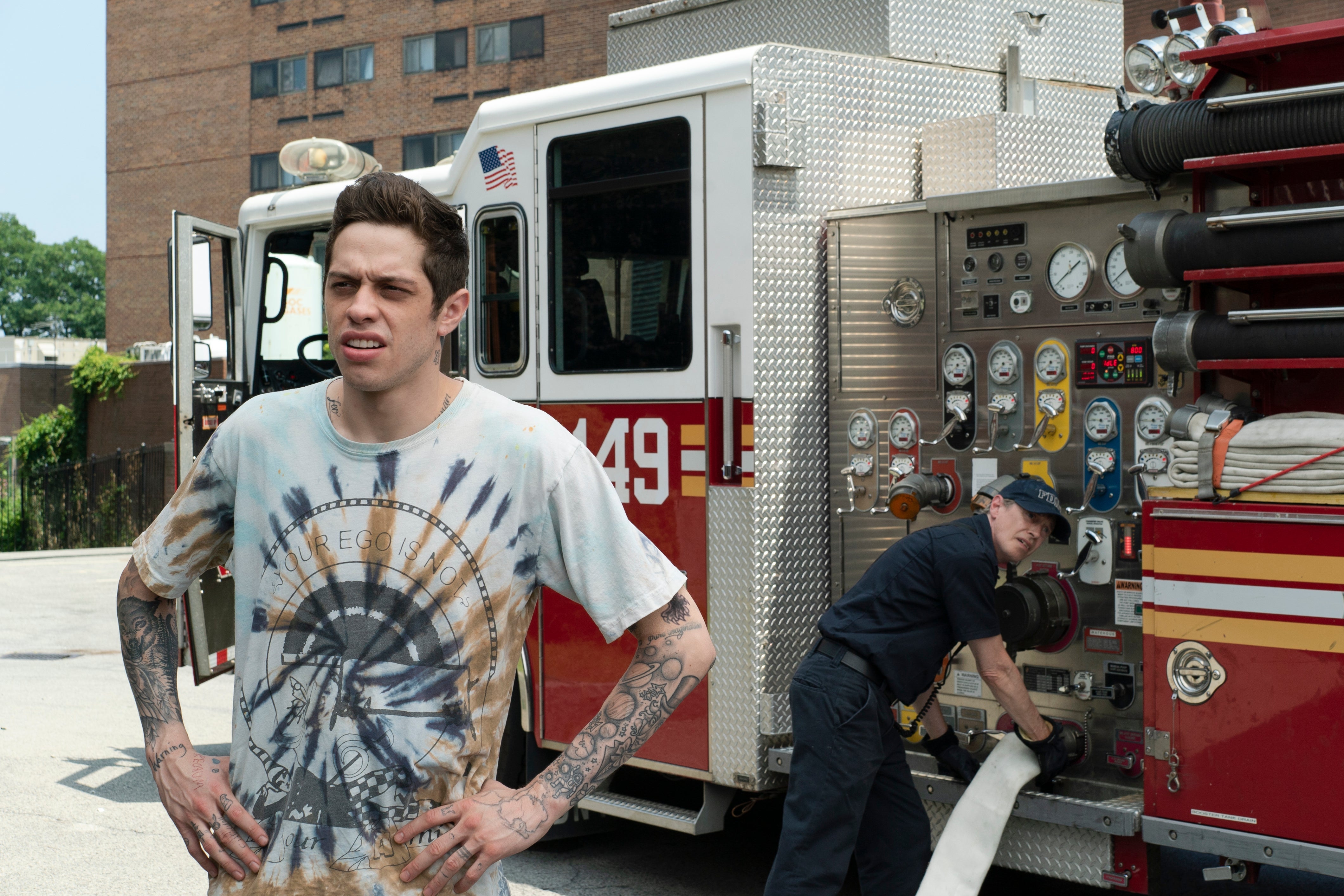 Pete Davidson, hands on hips, stands outside of a firehouse.