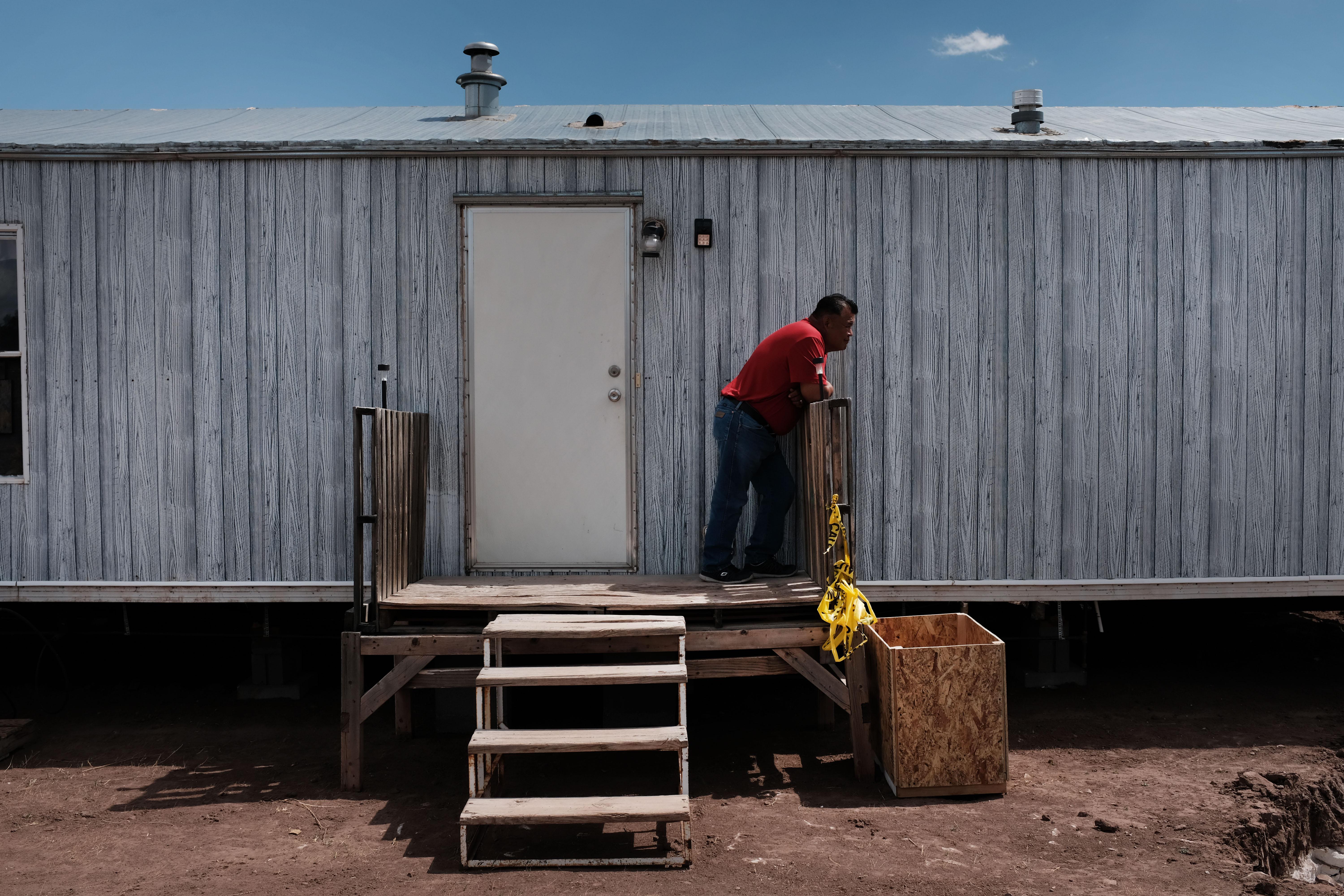 A man leans on a wooden platform by the door of a mobile home.