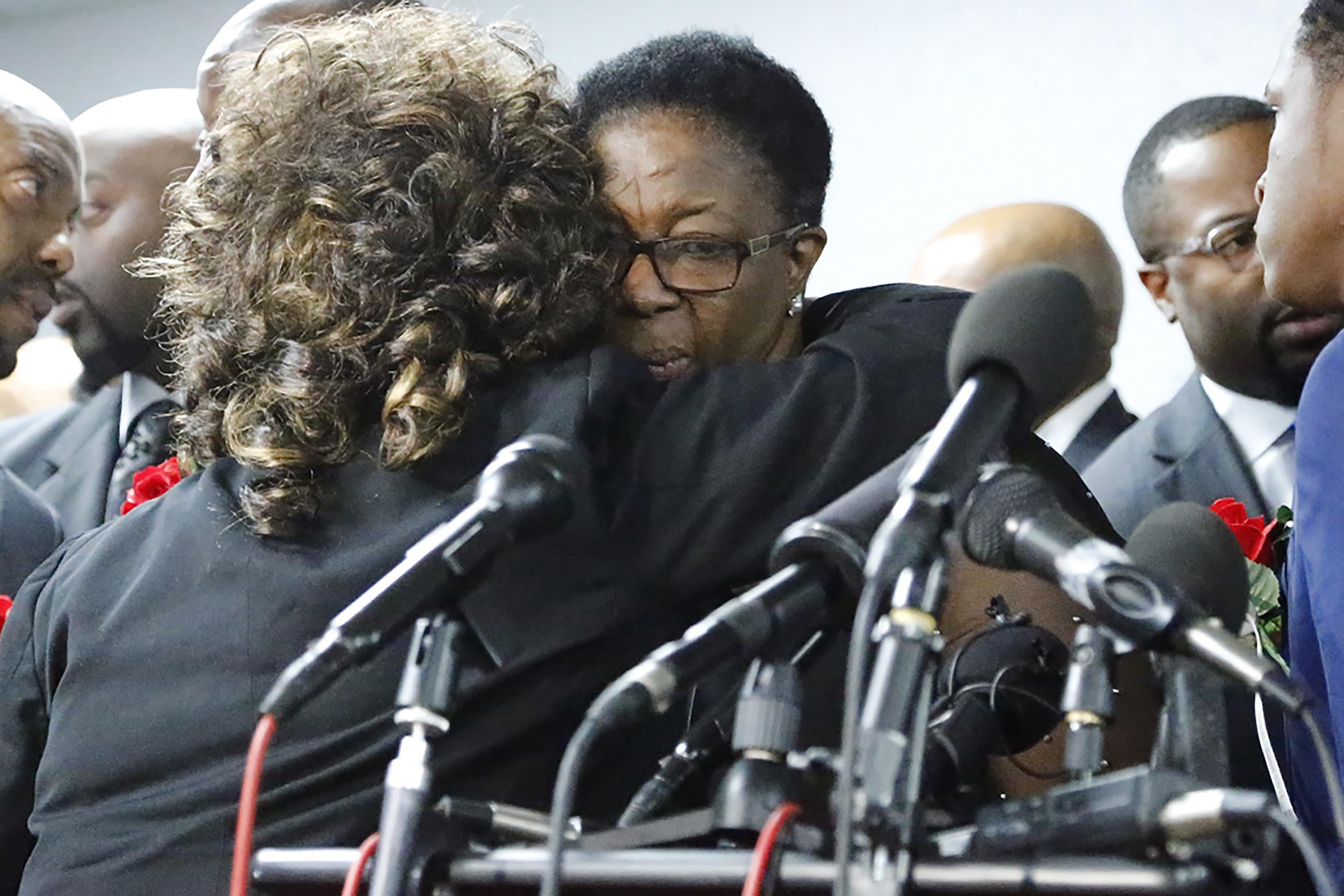 Allison Jean, Botham's mother, embraces a person with curly hair while standing in front of several microphones.