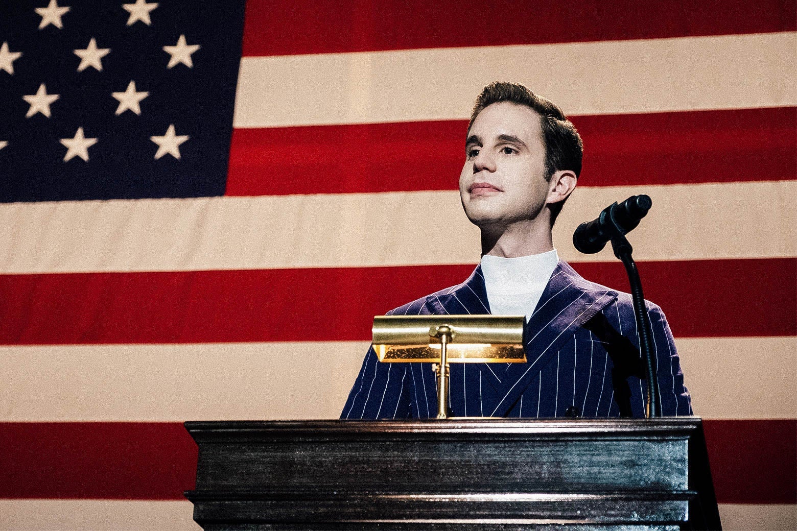 Ben Platt as Payton, standing at a podium in front of an American flag.