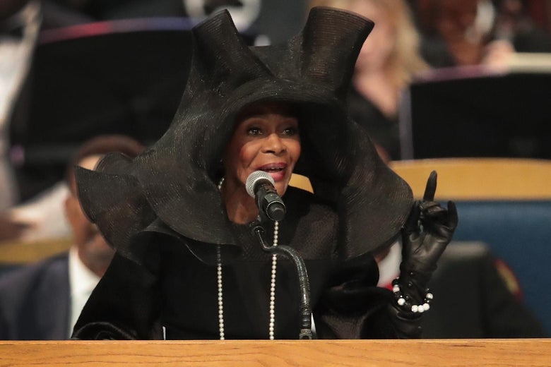 Cicely Tyson speaks at a podium at Aretha Franklin's funeral in a gigantic black floppy hat. 