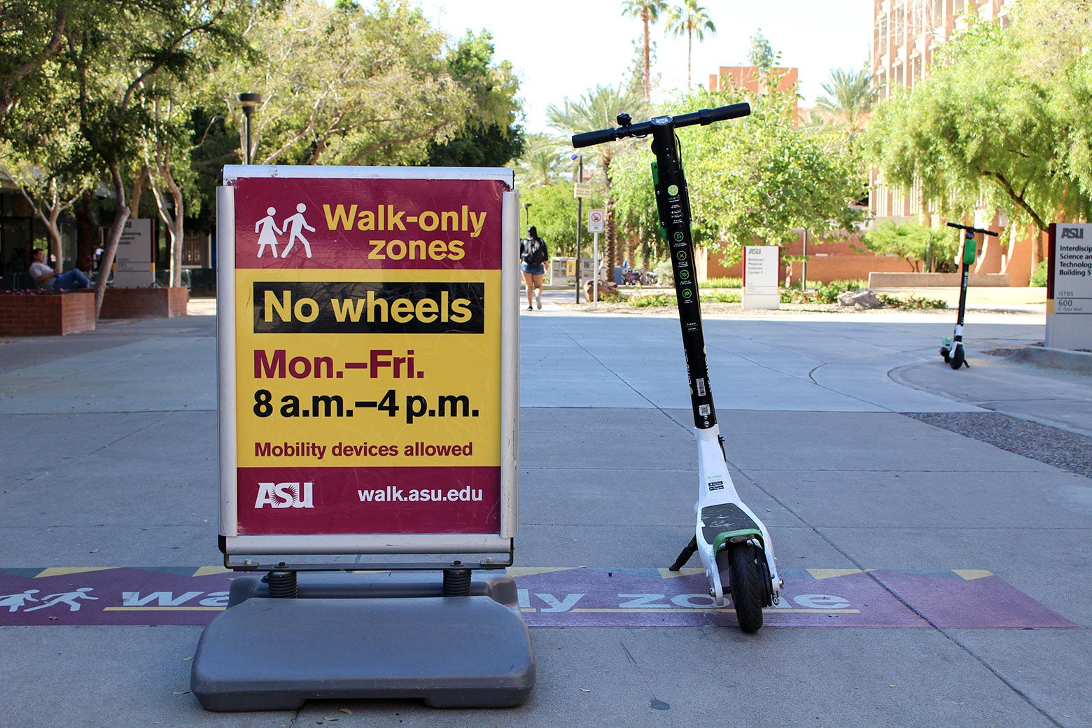 An electric scooter is next to a sign at ASU that says "Walk-Only Zones / No Wheels"