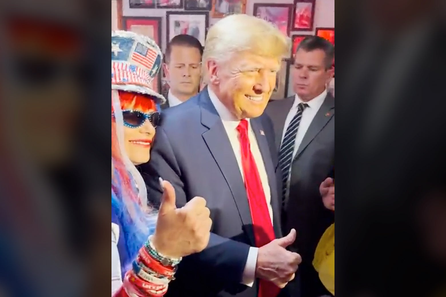 A still image from a video in which Trump and Larson-Olson, who is wearing a red, white, and blue hat and has similarly colored streamers in her hair and bracelets on her wrist, give thumbs up gestures.