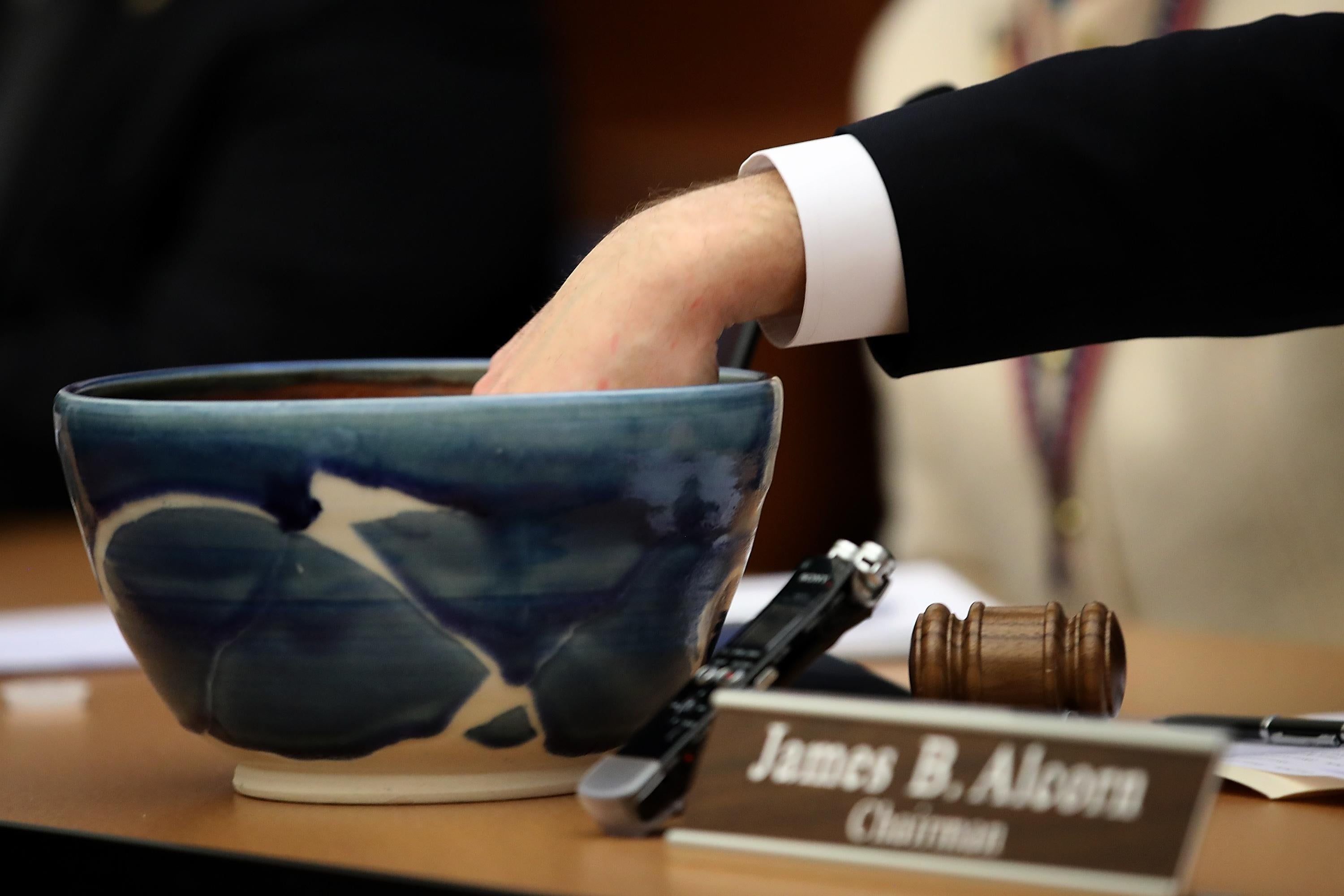 A lawmaker pulls a slip of paper out of a ceramic bowl.