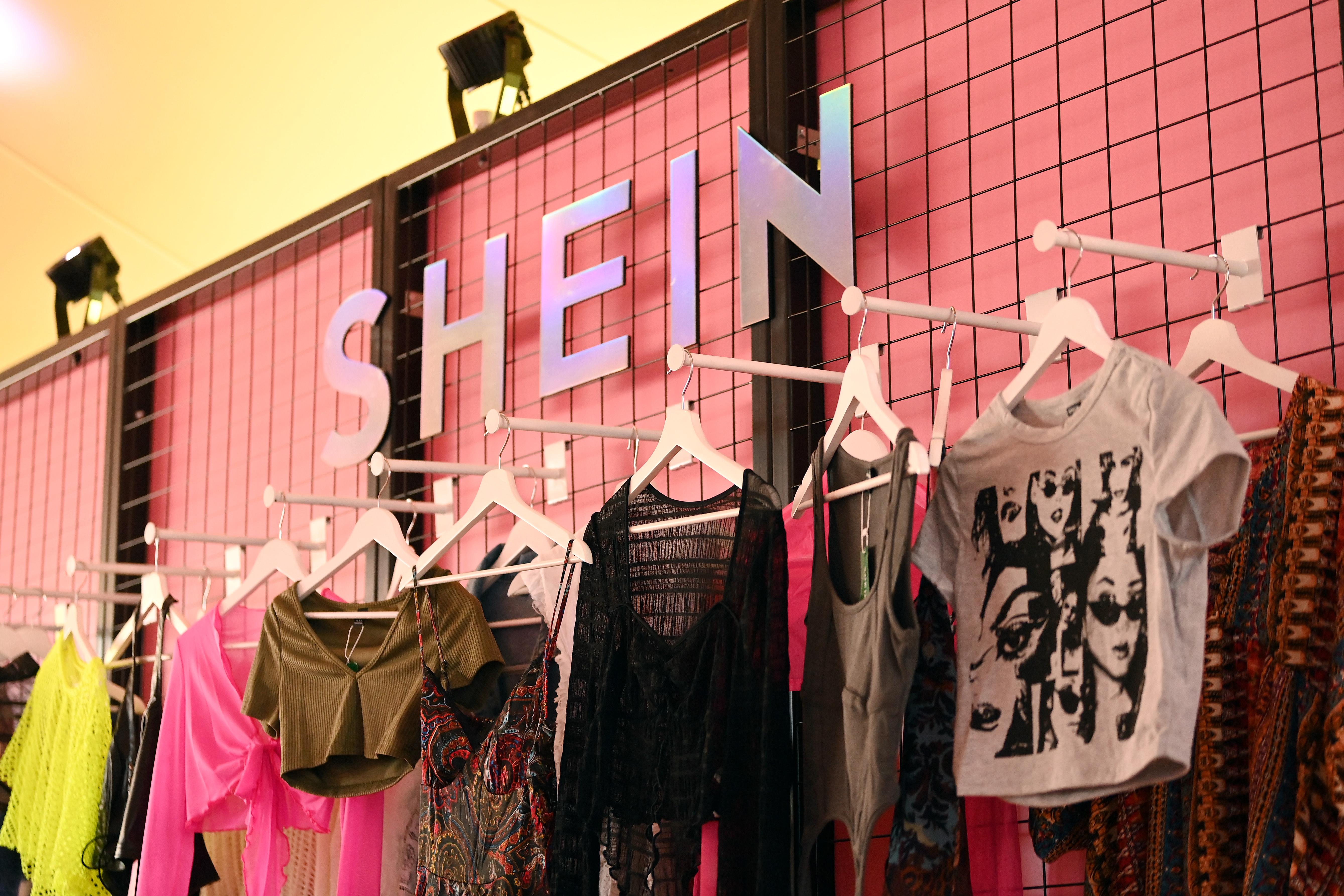Crop tops in various colors and styles hang on a pink wall. Above them is a sign that says "SHEIN." 