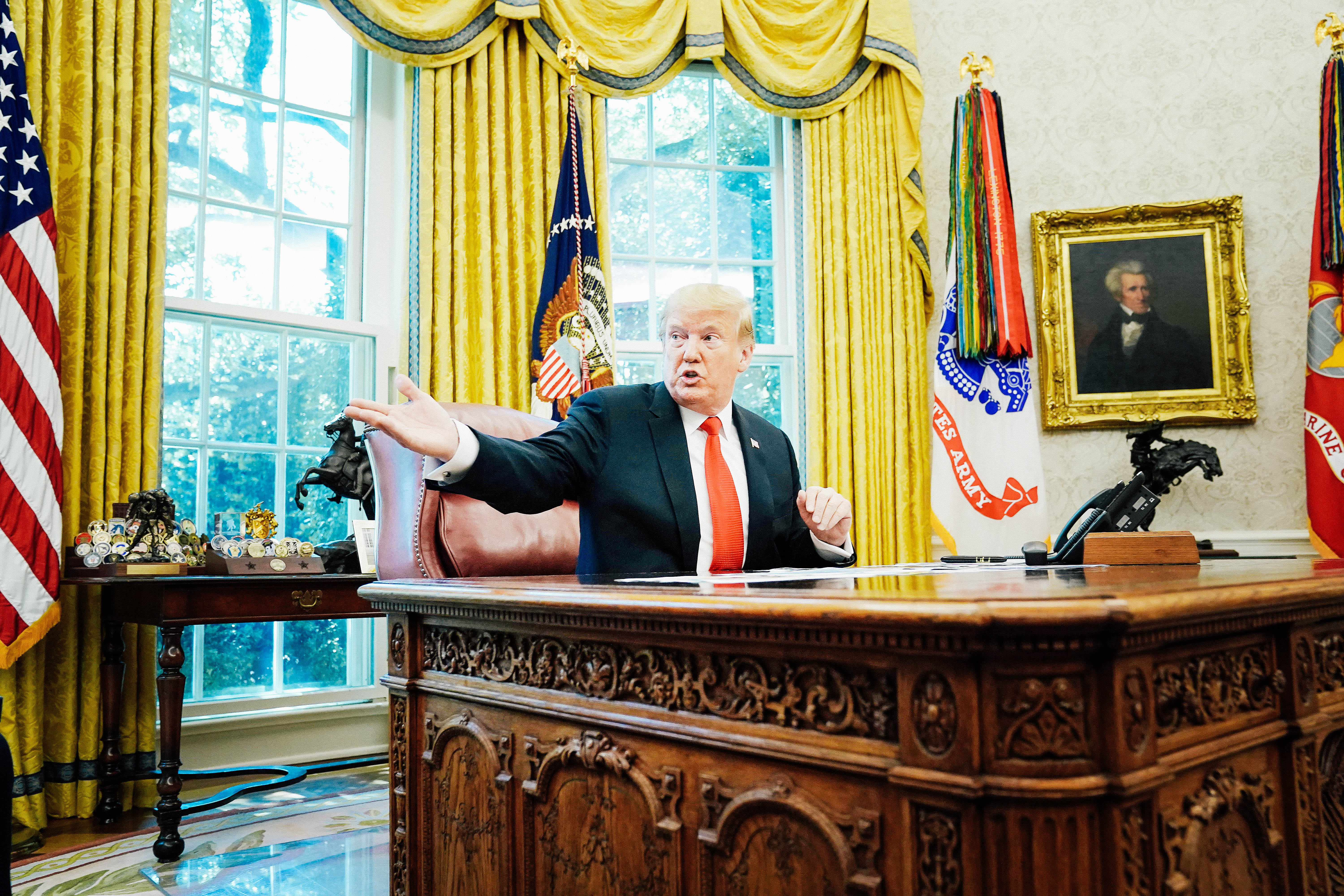 Donald Trump gestures while sitting at his desk in the Oval Office.
