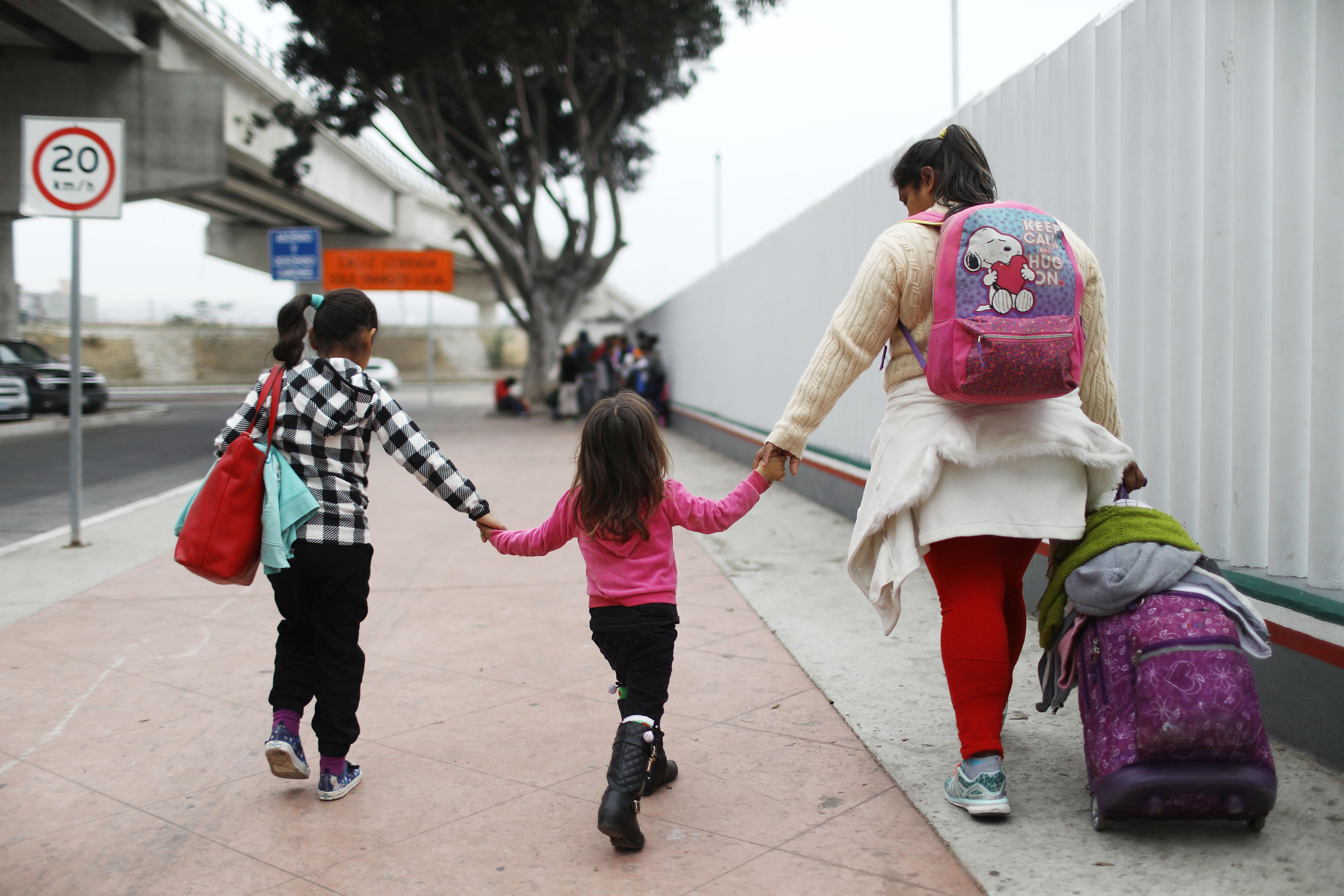 A migrant mother walks with her two daughters and their baggage along a border fence on their way to the port of entry to ask for asylum in the U.S. 