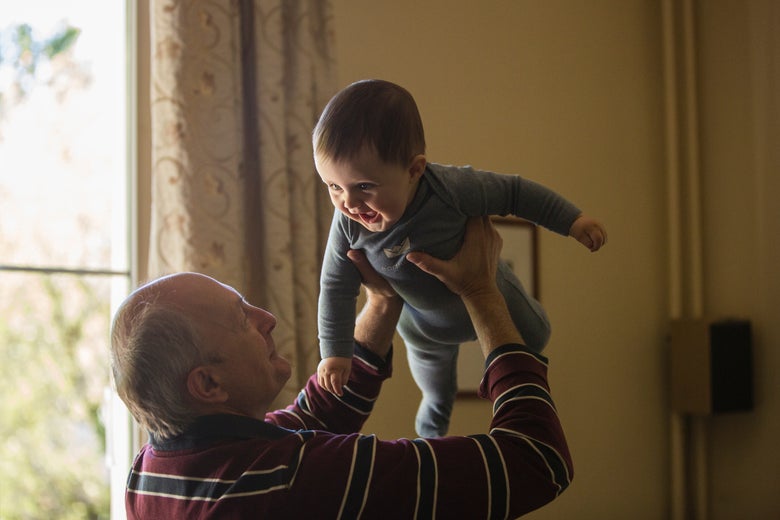 A grandfather holds a smiling baby up in the air.