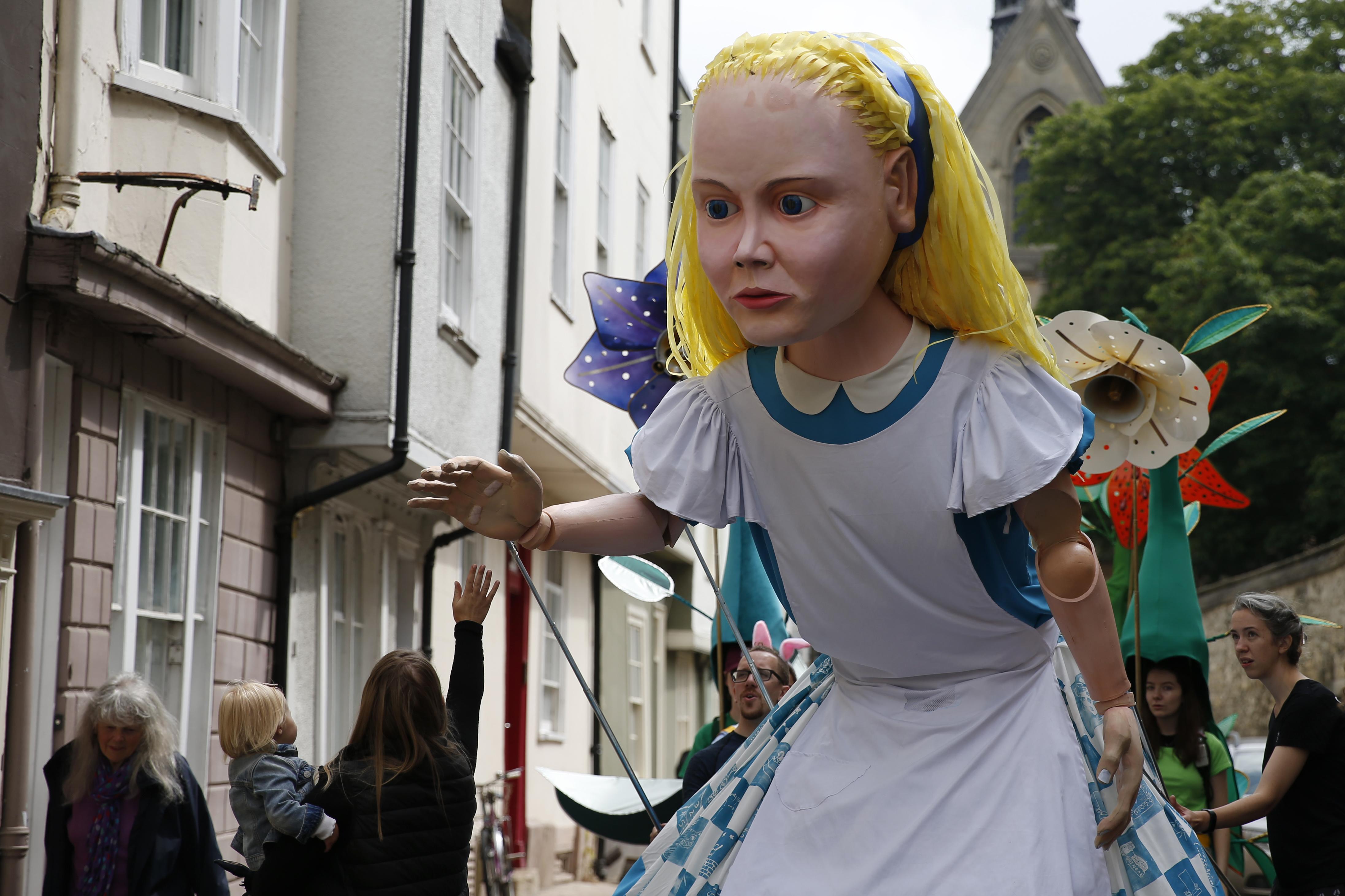 OXFORD, ENGLAND - JULY 03: An Alice in Wonderland puppet gestures to a child between performances on July 3, 2021 in Oxford, England. This year is the 150th anniversary of author Lewis Carroll's Through the Looking Glass, the sequel to Alice in Wonderland. The Alice's Day celebrations feature a 3.25 metre tall Alice puppet accompanied by huge talking flowers operated by puppeteers and an array of Alice in Wonderland characters that will roam the streets of Oxford interacting with the public. (Photo by Hollie Adams/Getty Images)