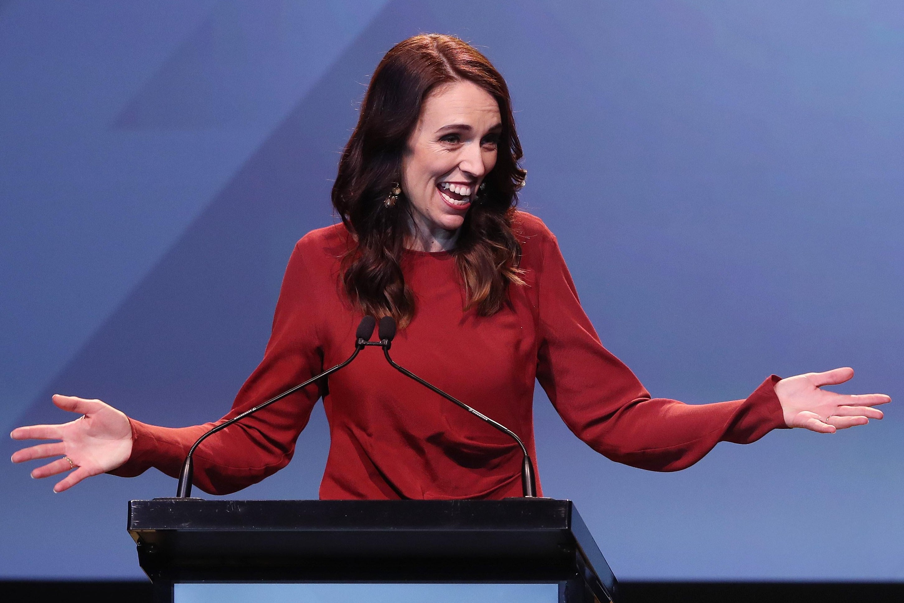 Jacinda Ardern holds her hands out wide as she speaks from behind a podium.