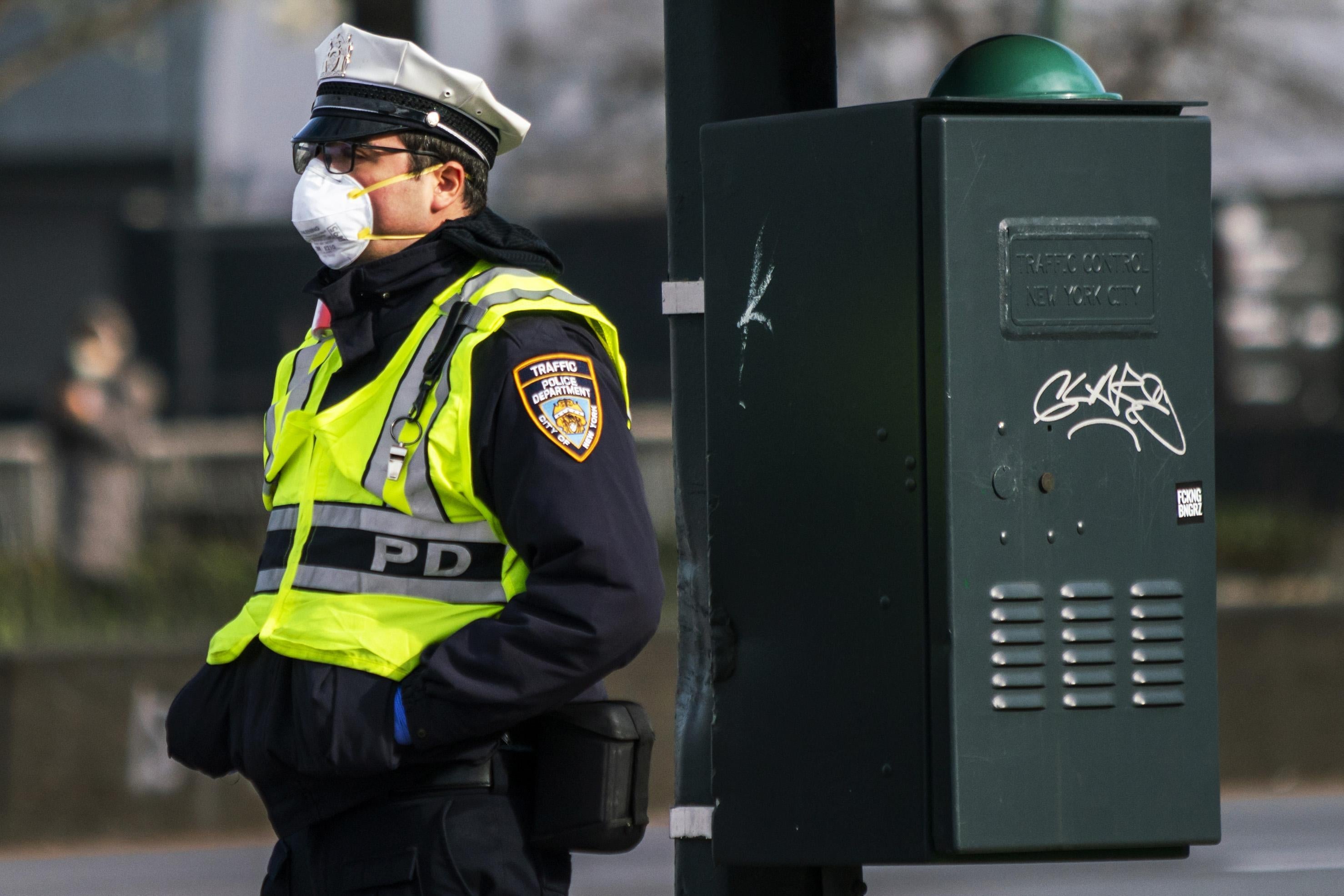 A police officer wearing a face mask and a safety vest directs traffic on the street.
