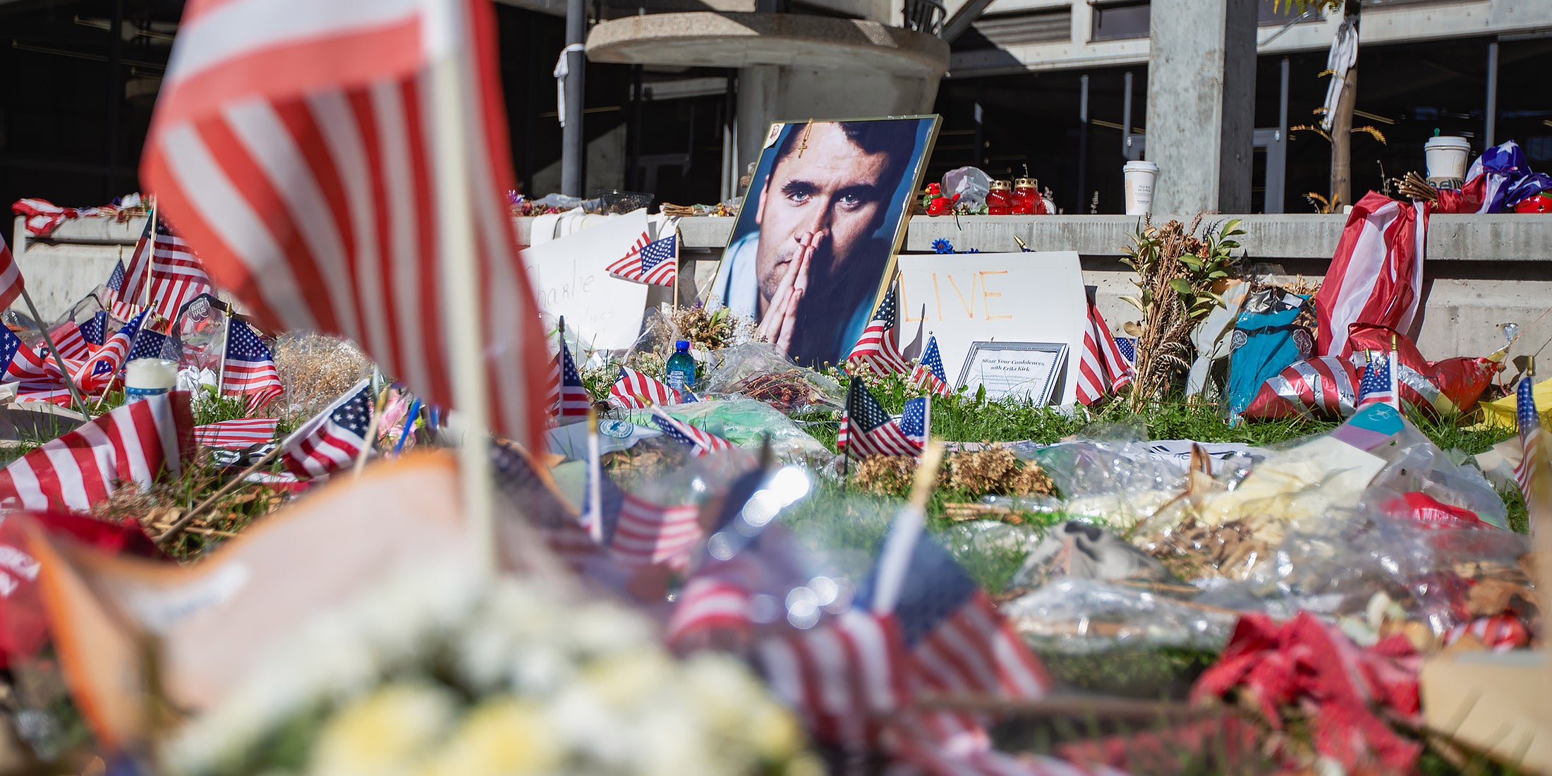 A memorial to Charlie Kirk with flags, flowers, and pictures of him. 