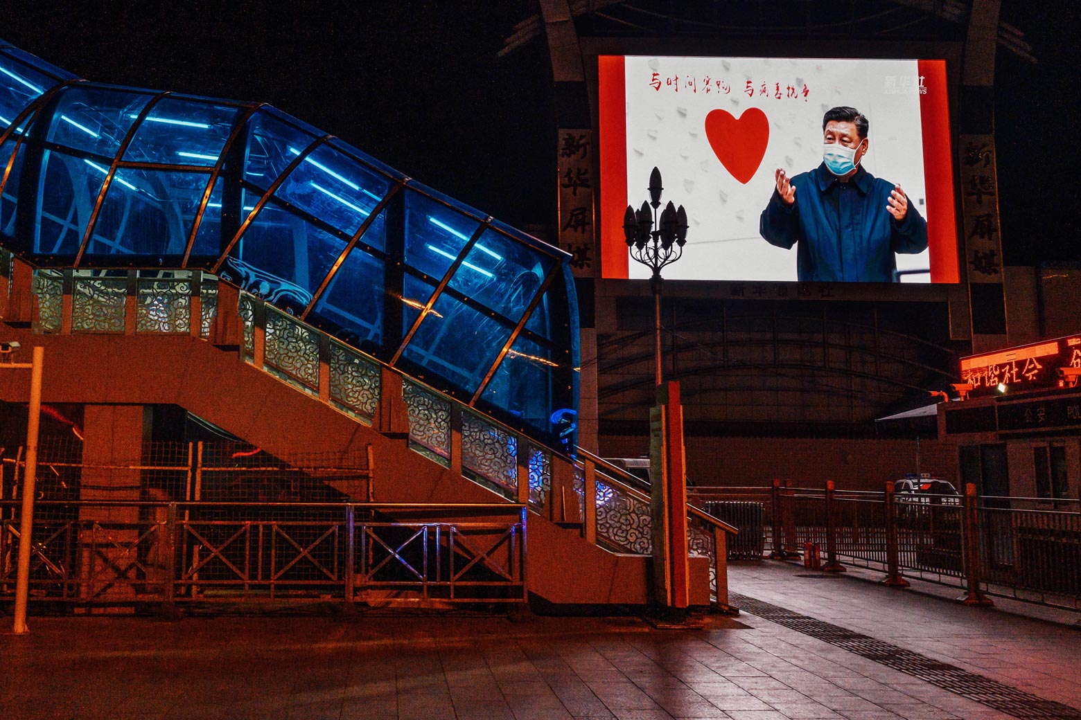 Outside a nearly empty railway station, a large monitor shows an image of Chinese President Xi Jinping wearing a mask next to a heart.